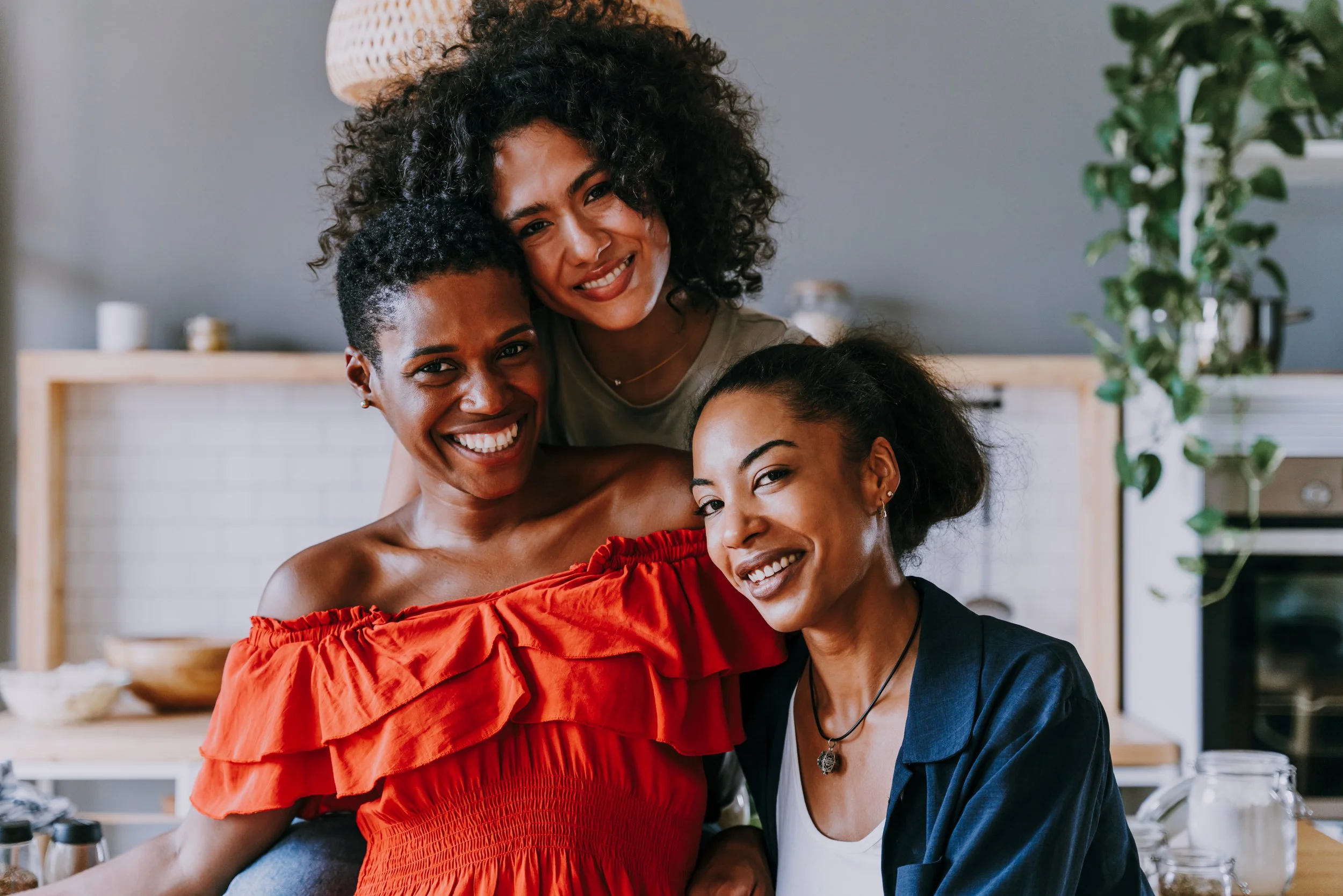 Three women smiling and posing together in a cozy kitchen.