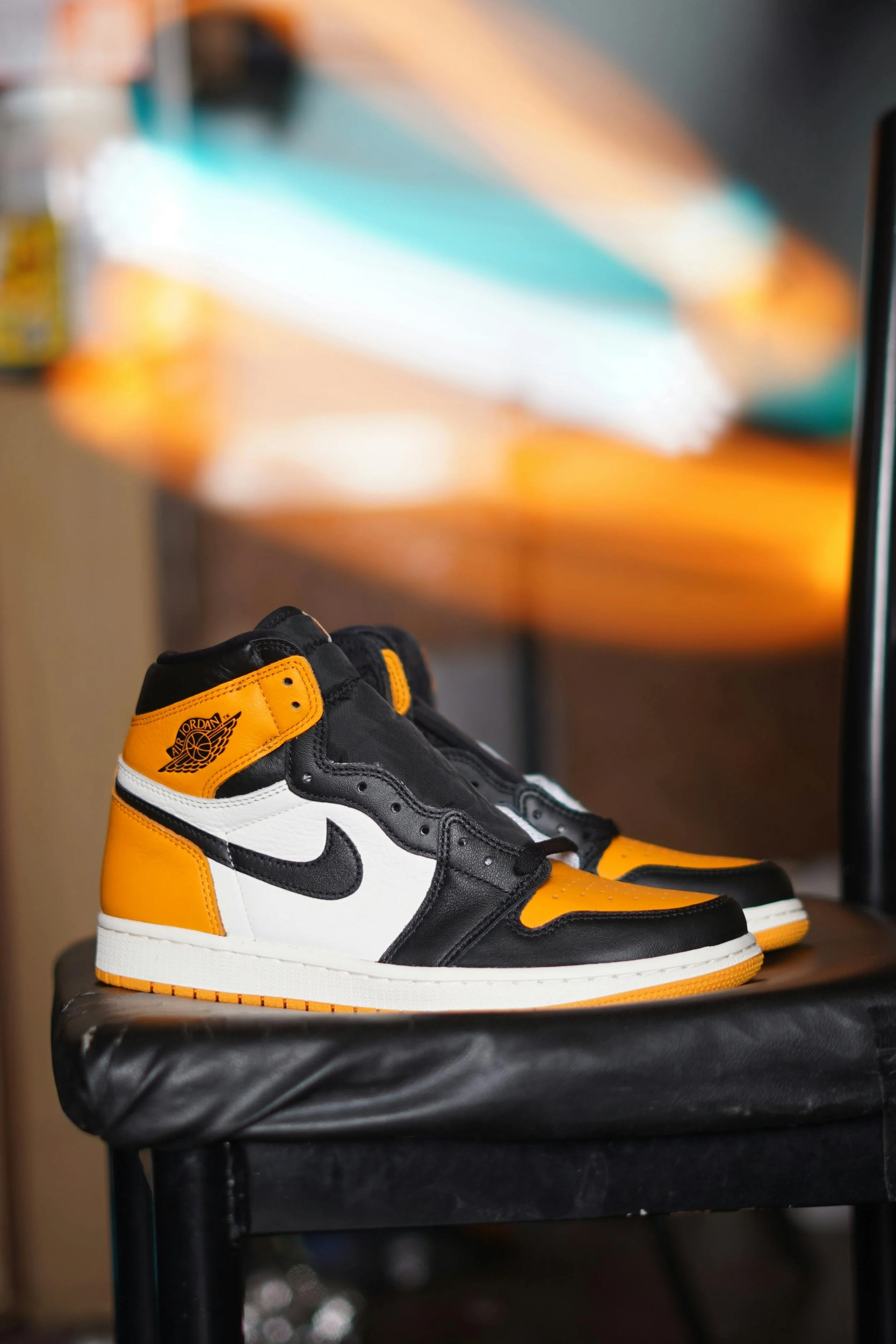 A pair of black, white, and orange Air Jordan 1 sneakers on a black surface with a blurred background.
