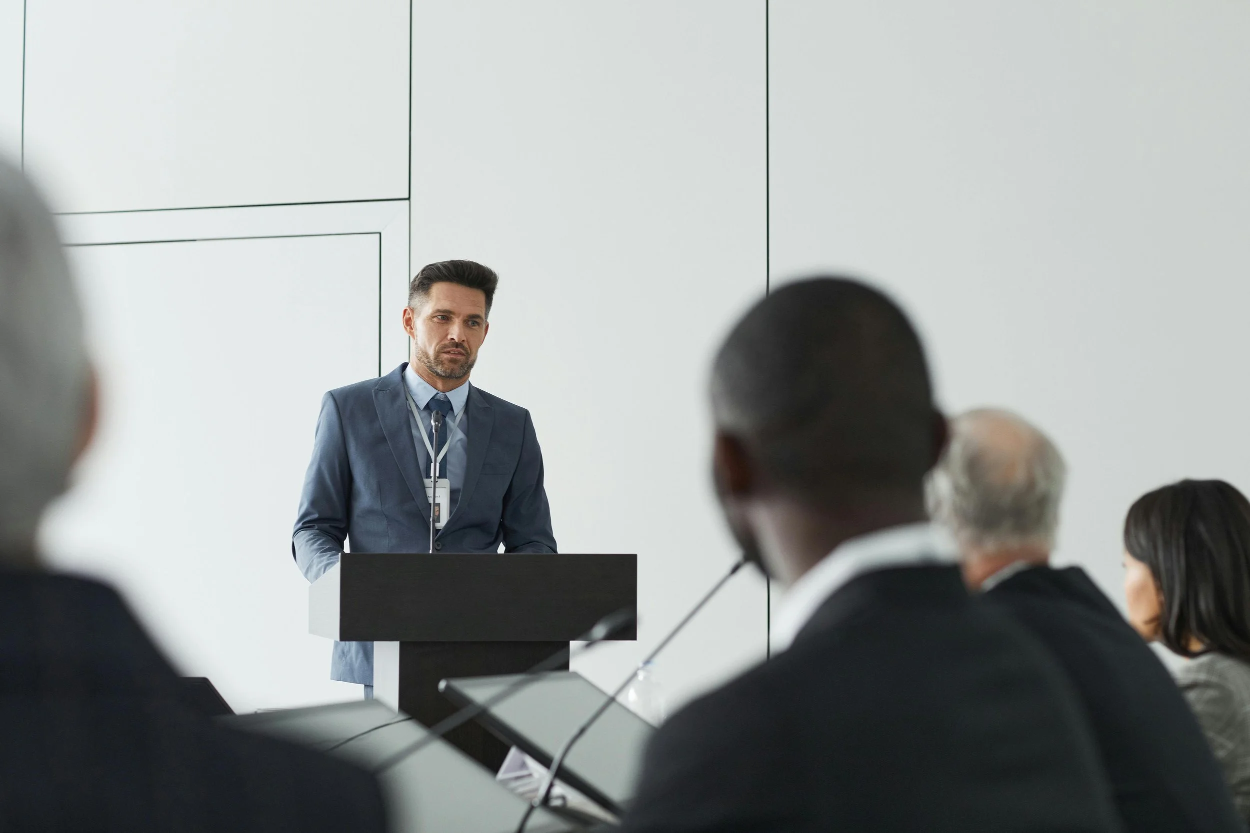 A man in a suit standing at a podium giving a presentation to a group in a conference room.