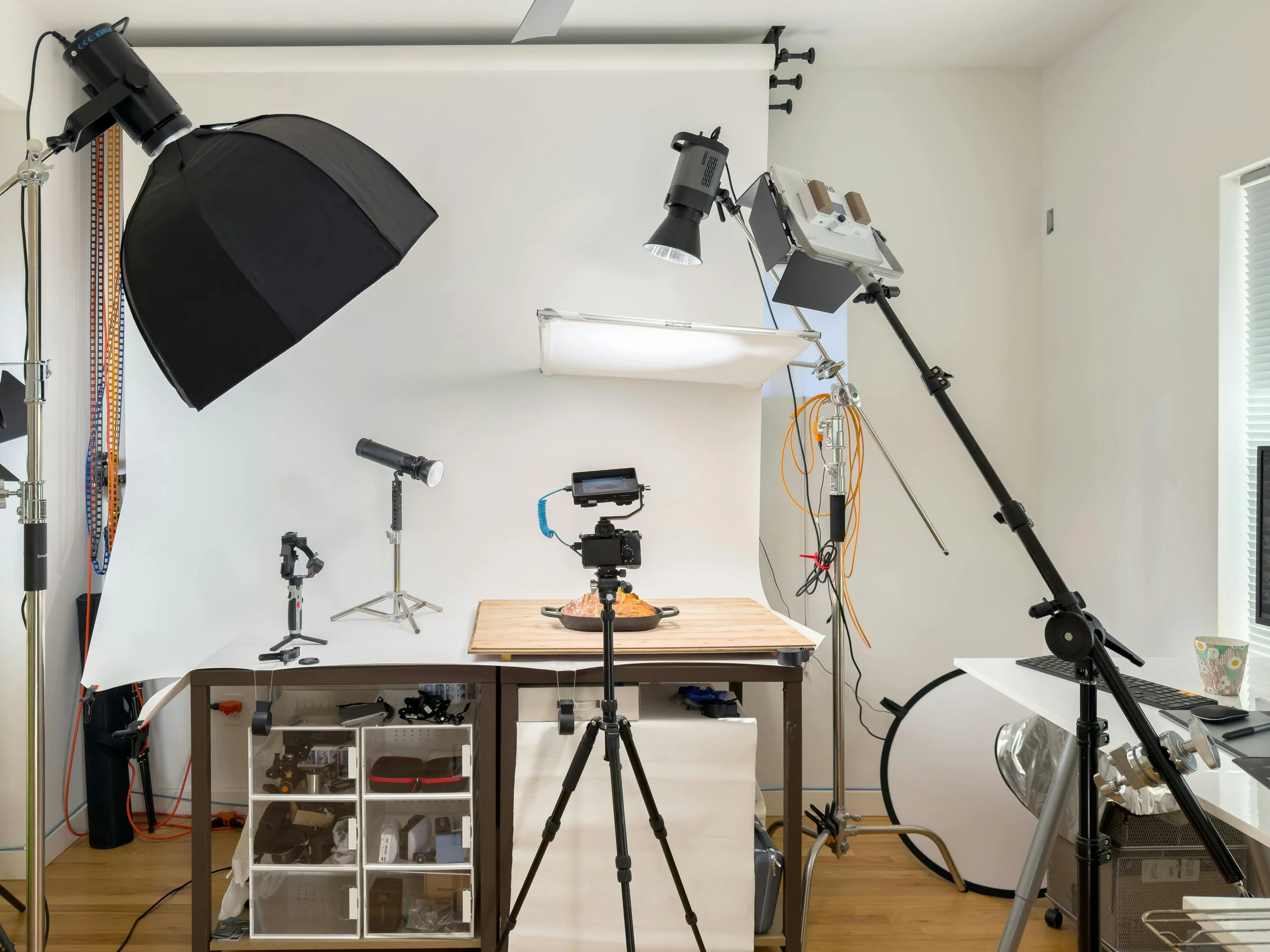 Photography studio setup with lighting equipment, camera on tripod, backdrop, and food props on a table.