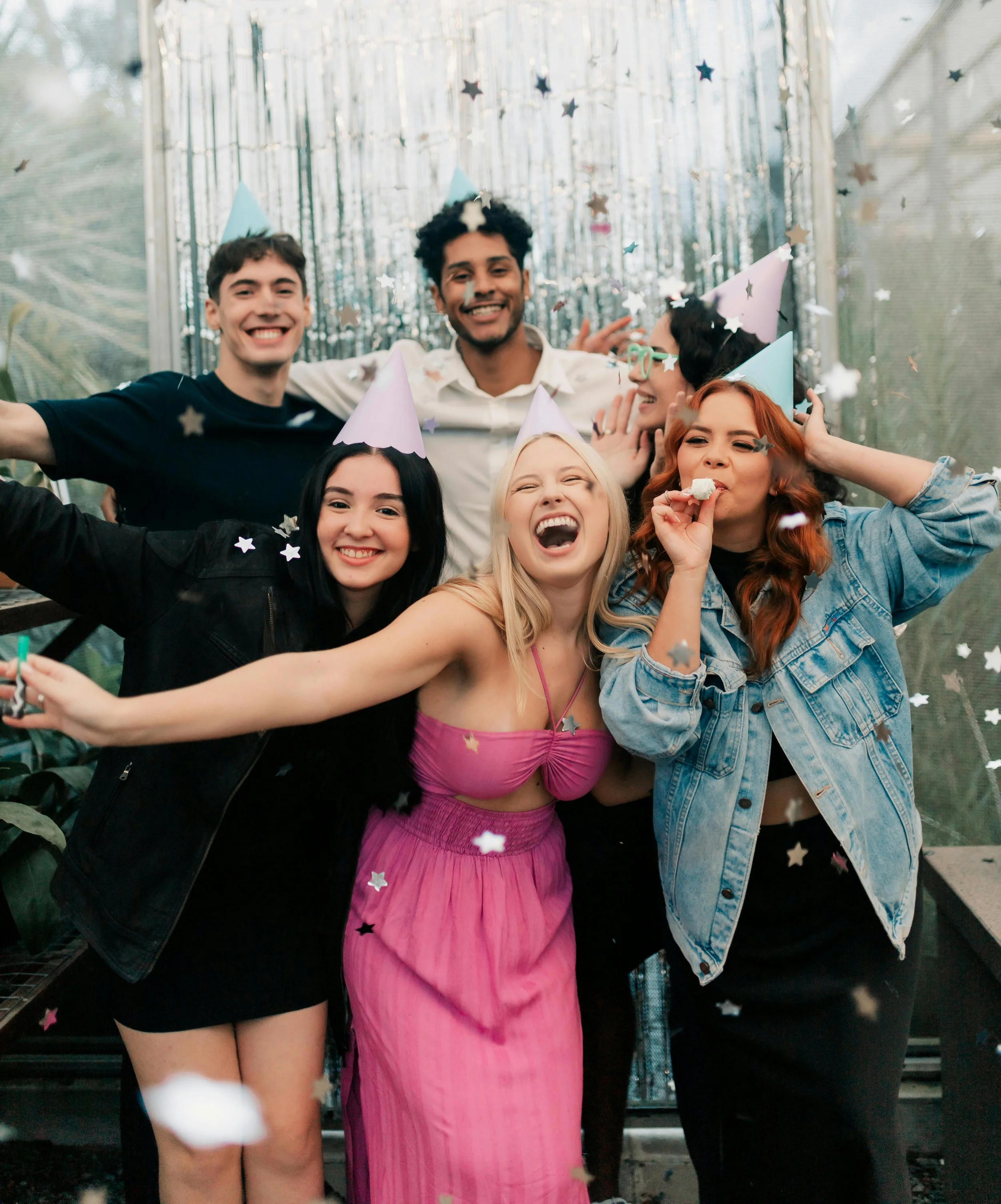 Group of young friends celebrating at a party with confetti, party hats, and joyful expressions.