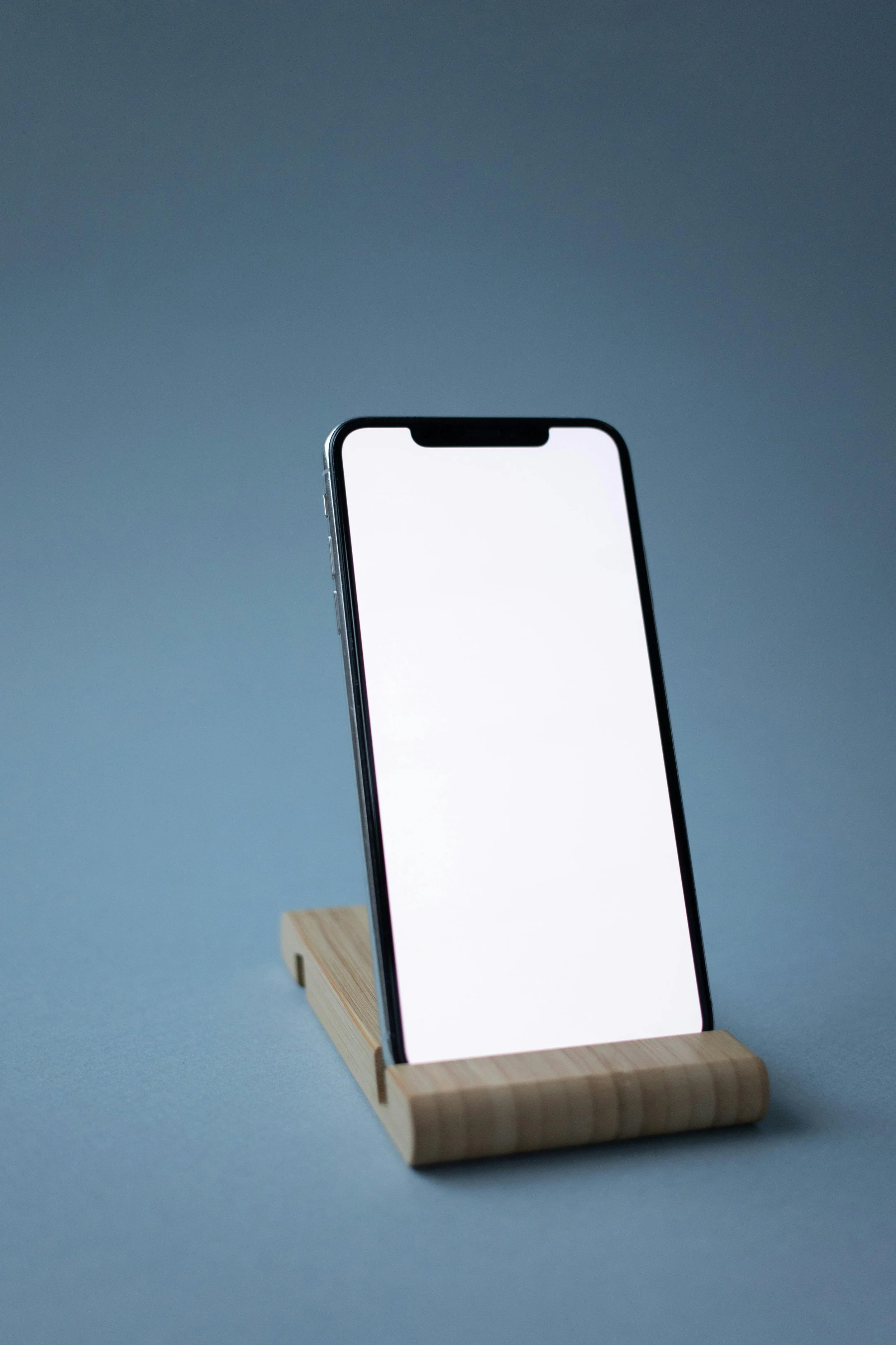 Smartphone with a blank white screen on a wooden stand against a blue background.