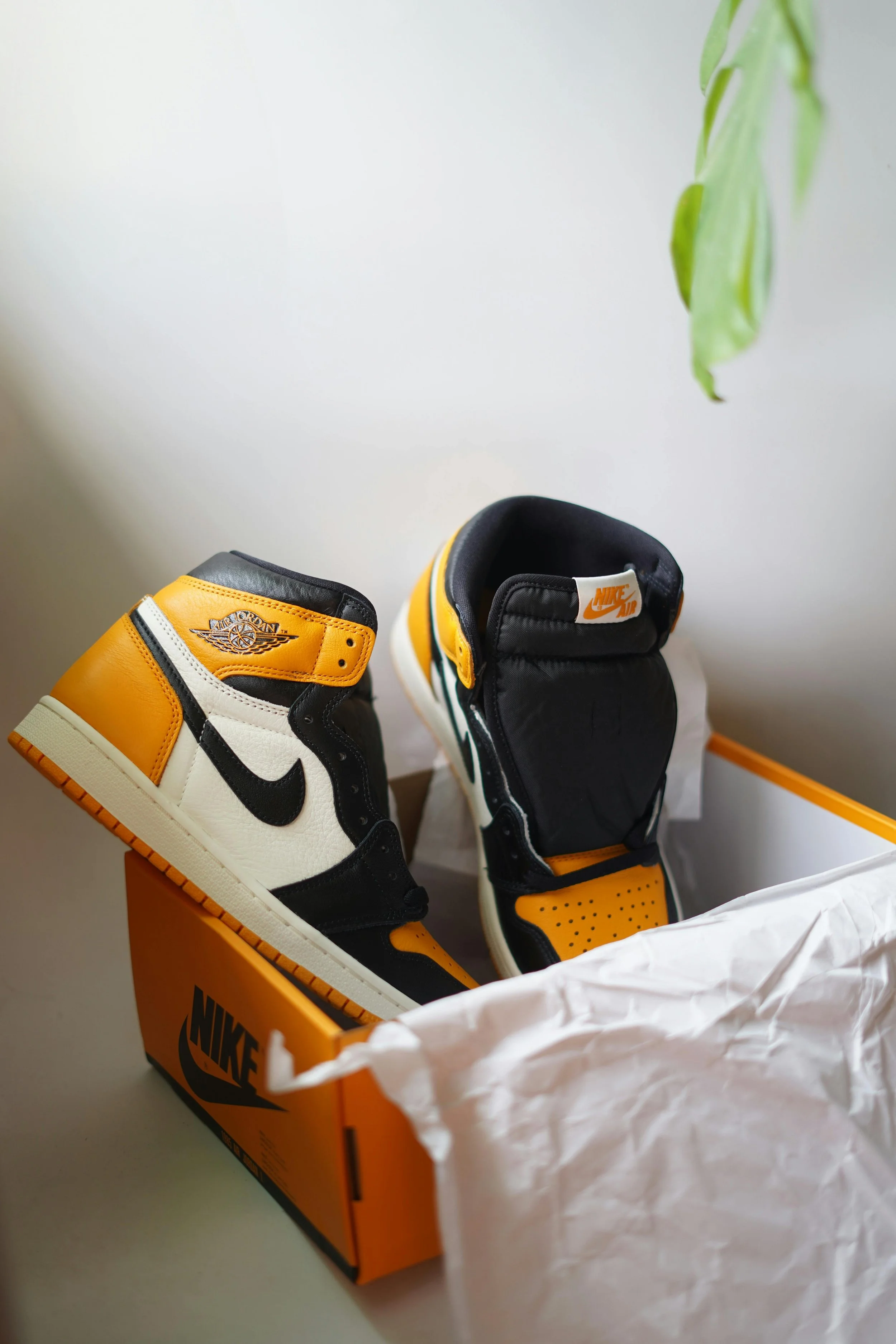 Pair of Nike Air Jordan sneakers in black, white, yellow, and orange colors in a Nike shoe box, with tissue paper partially covering the shoes.