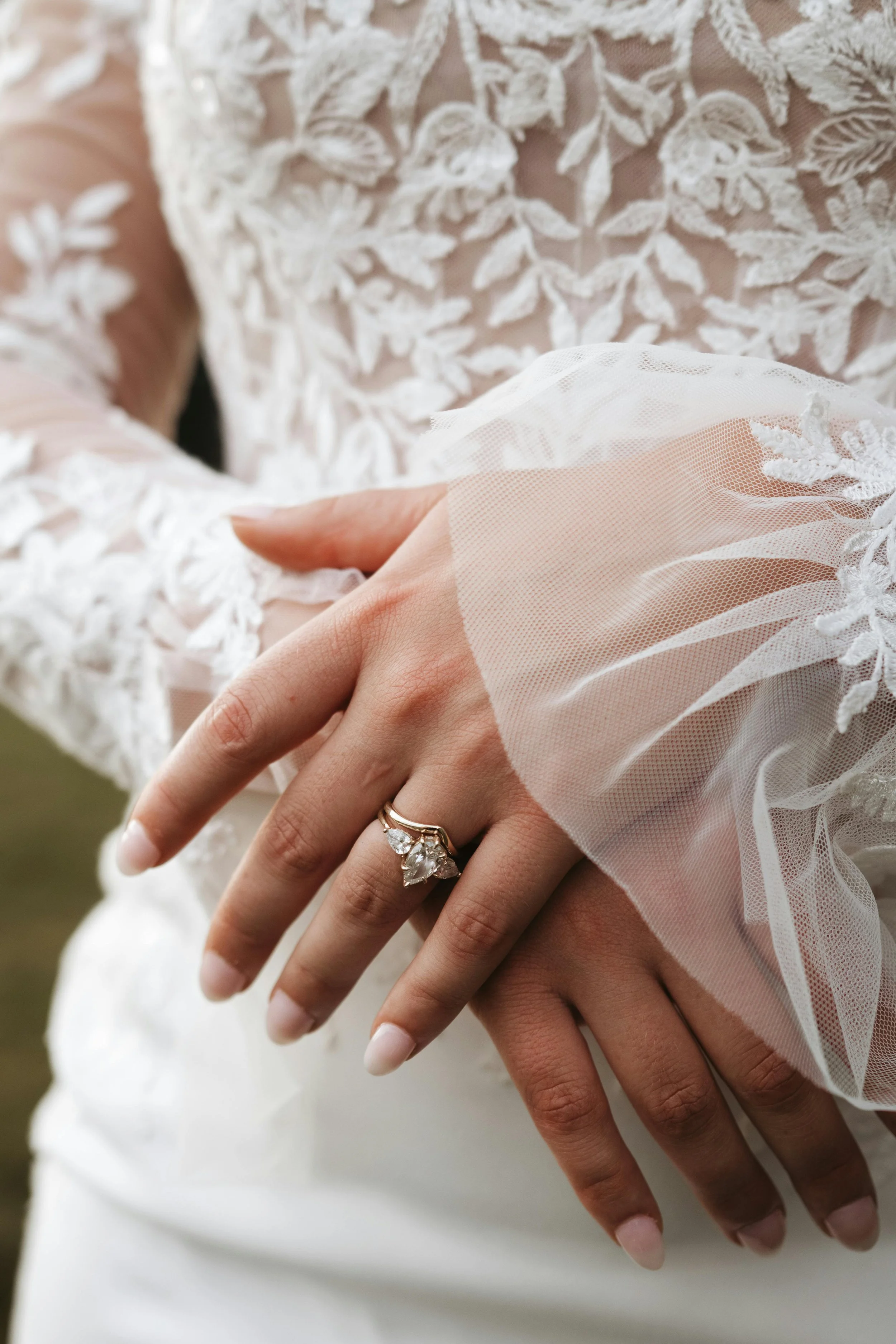 Close-up of a woman wearing a wedding dress showing her left hand with a diamond engagement ring.
