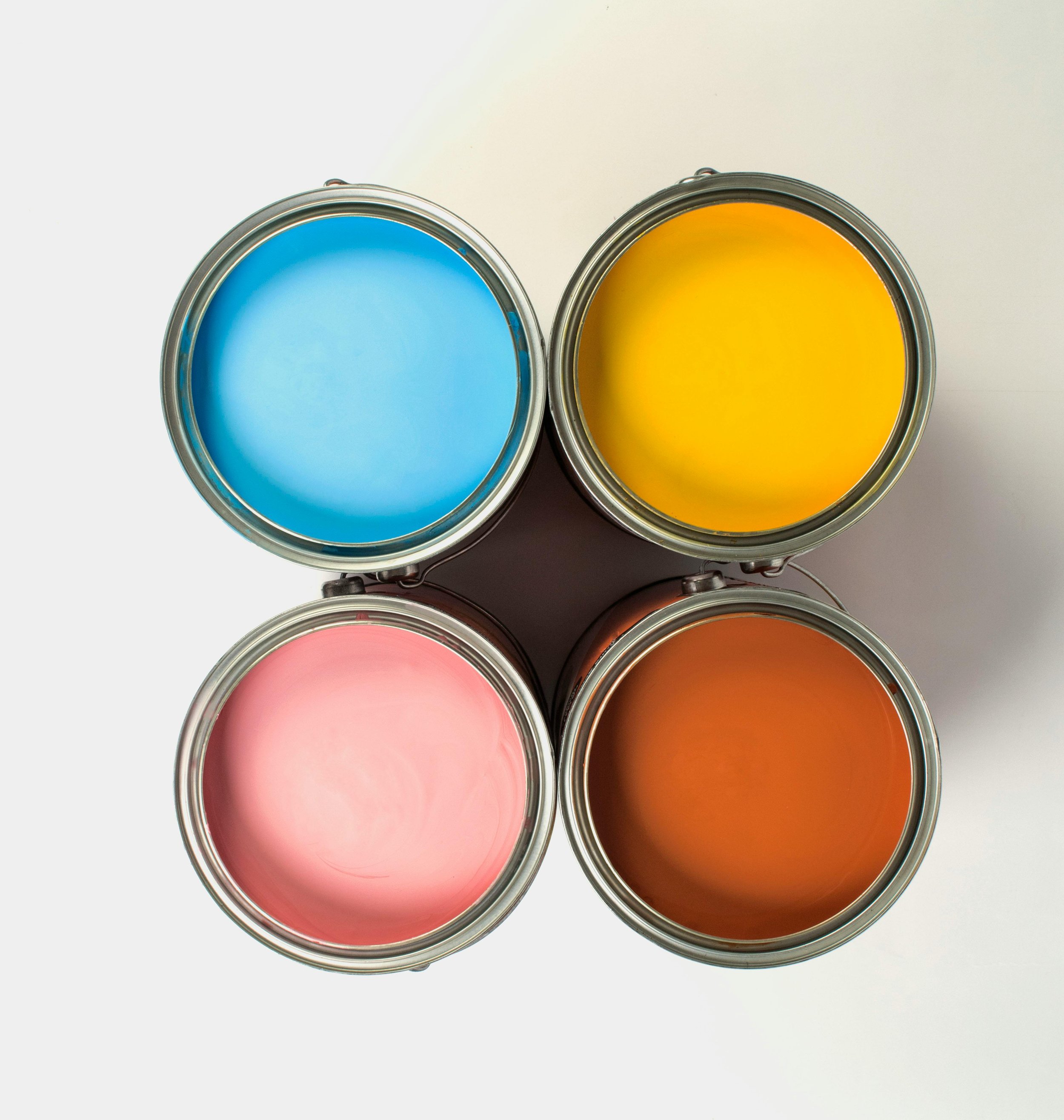 Four open cans of paint viewed from above, with blue, yellow, pink, and orange colors.