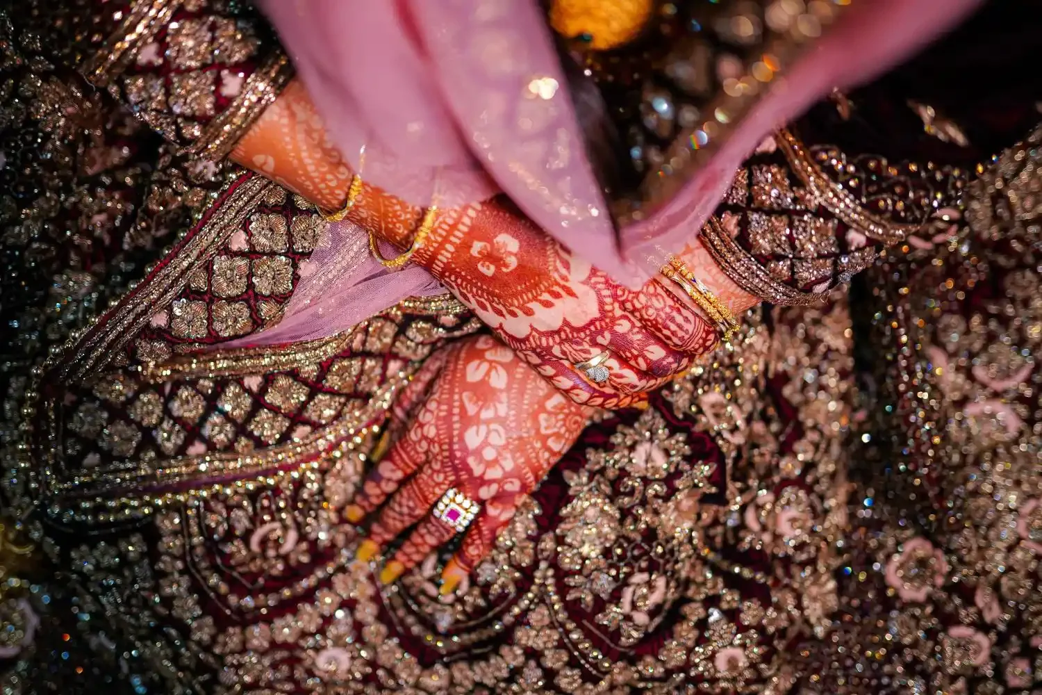 Close-up of intricately embroidered and beaded textile fabric in black, pink, gold, red, orange, and brown colors, likely part of traditional or ceremonial clothing.