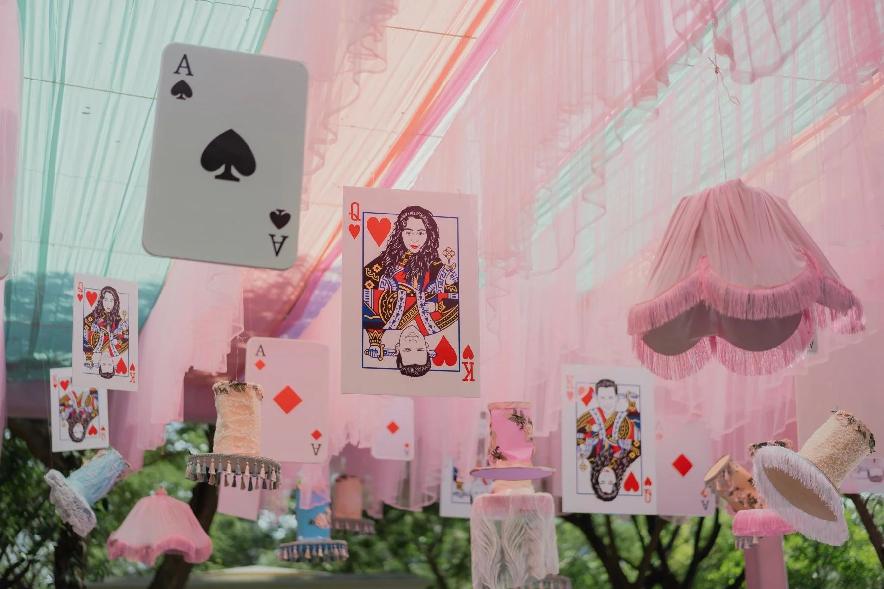 Pink outdoor canopy decorated with playing cards featuring a Queen of Hearts and Ace of Diamonds, and pink lampshades with fringe, creating a festive, whimsical atmosphere.