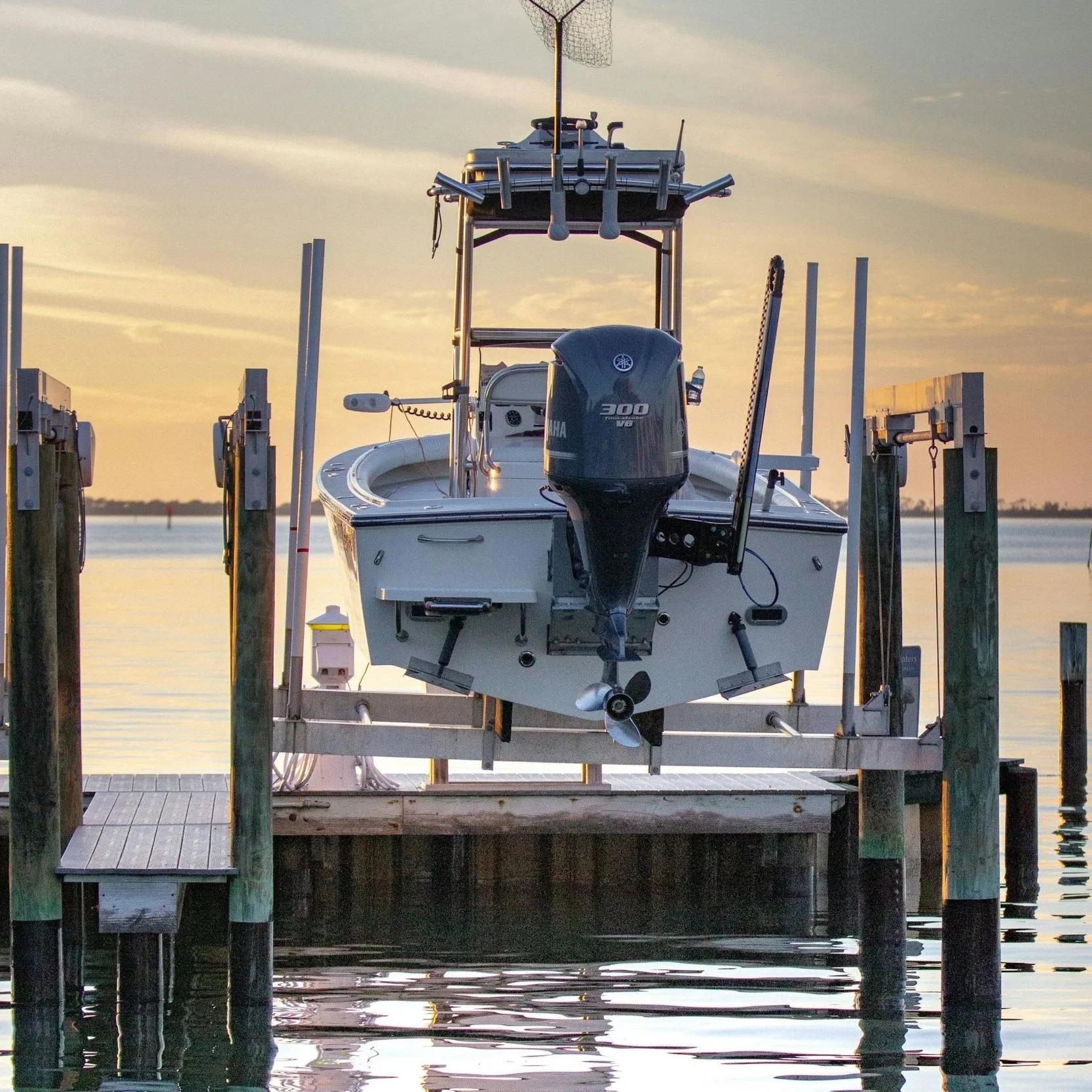 A boat docked at a wooden pier during sunset, with a Sun Yamaha outboard motor, and a fishing tower with antennas and equipment on top.