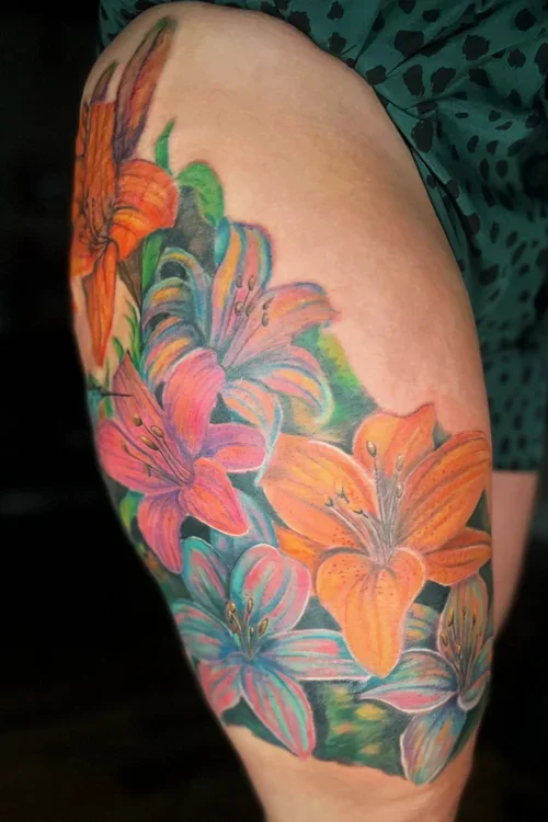 Colorful tattoo of lilies in orange and pink on a person's upper arm