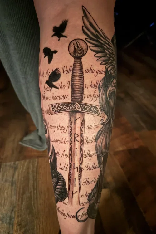 Tattoo of a sword with the inscription 'TRUST' on the blade, surrounded by birds, feathers, and script on a person's forearm.
