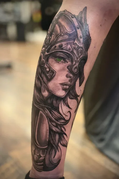 Tattoo of a woman with green eyes, wearing a medieval helmet, on a person's forearm.