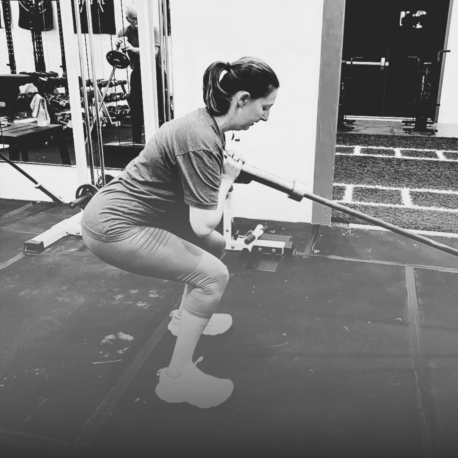 A woman in workout clothes performs a squat with a barbell in a gym.