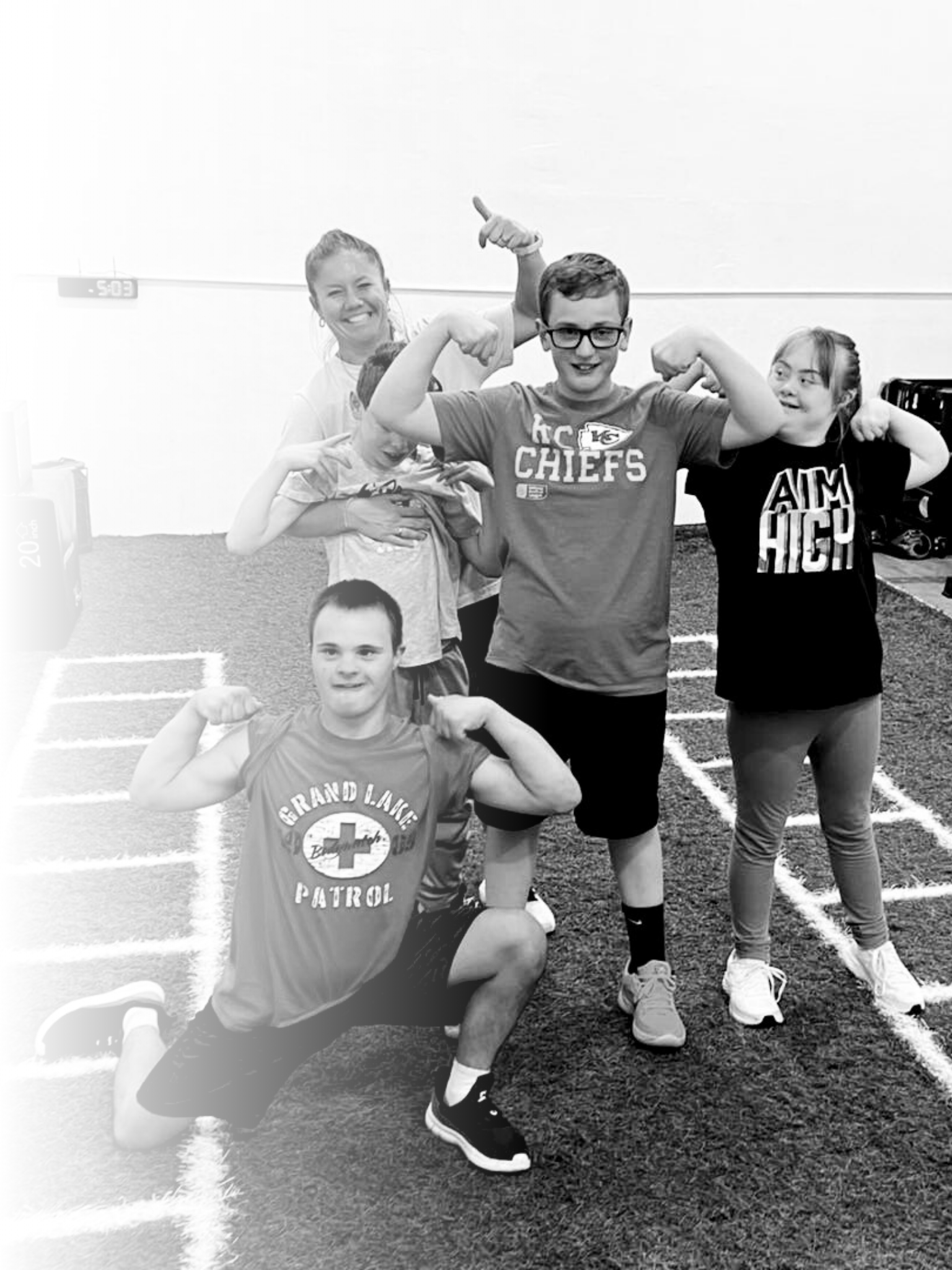 Group of five children posing and flexing muscles in a gym or sports facility with agility ladders on the floor.