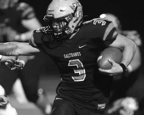 A football player in uniform holding a football while running on the field.