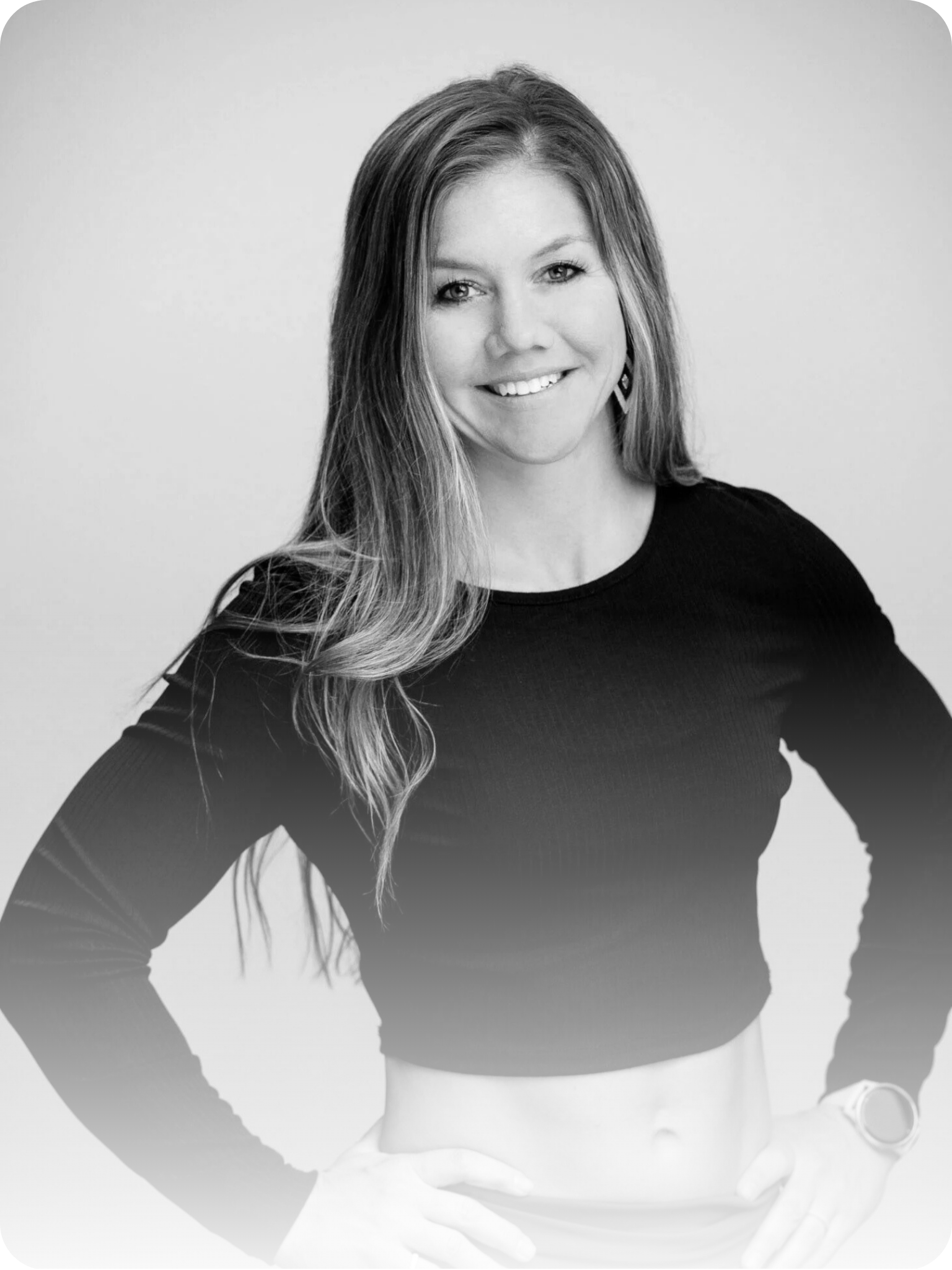Black and white photo of a smiling woman with long hair, wearing a long-sleeve crop top and a watch.