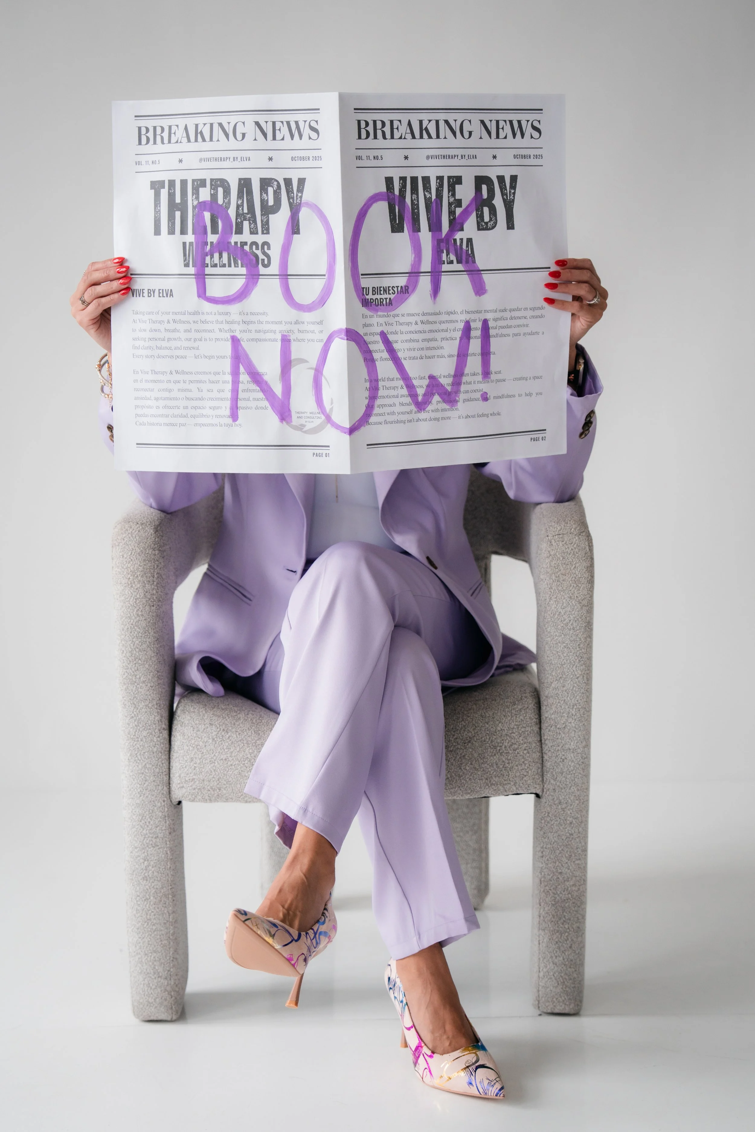 Person sitting in a chair, wearing a lavender suit and colorful high heels, holding a newspaper with purple graffiti on it that says "DO NOT DISTURB."