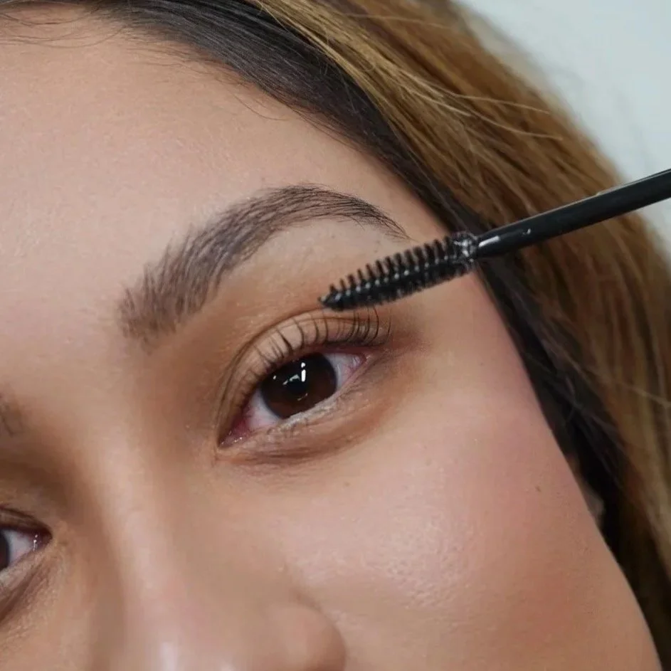 Close-up of a woman applying mascara to her eyelashes with a black mascara wand.