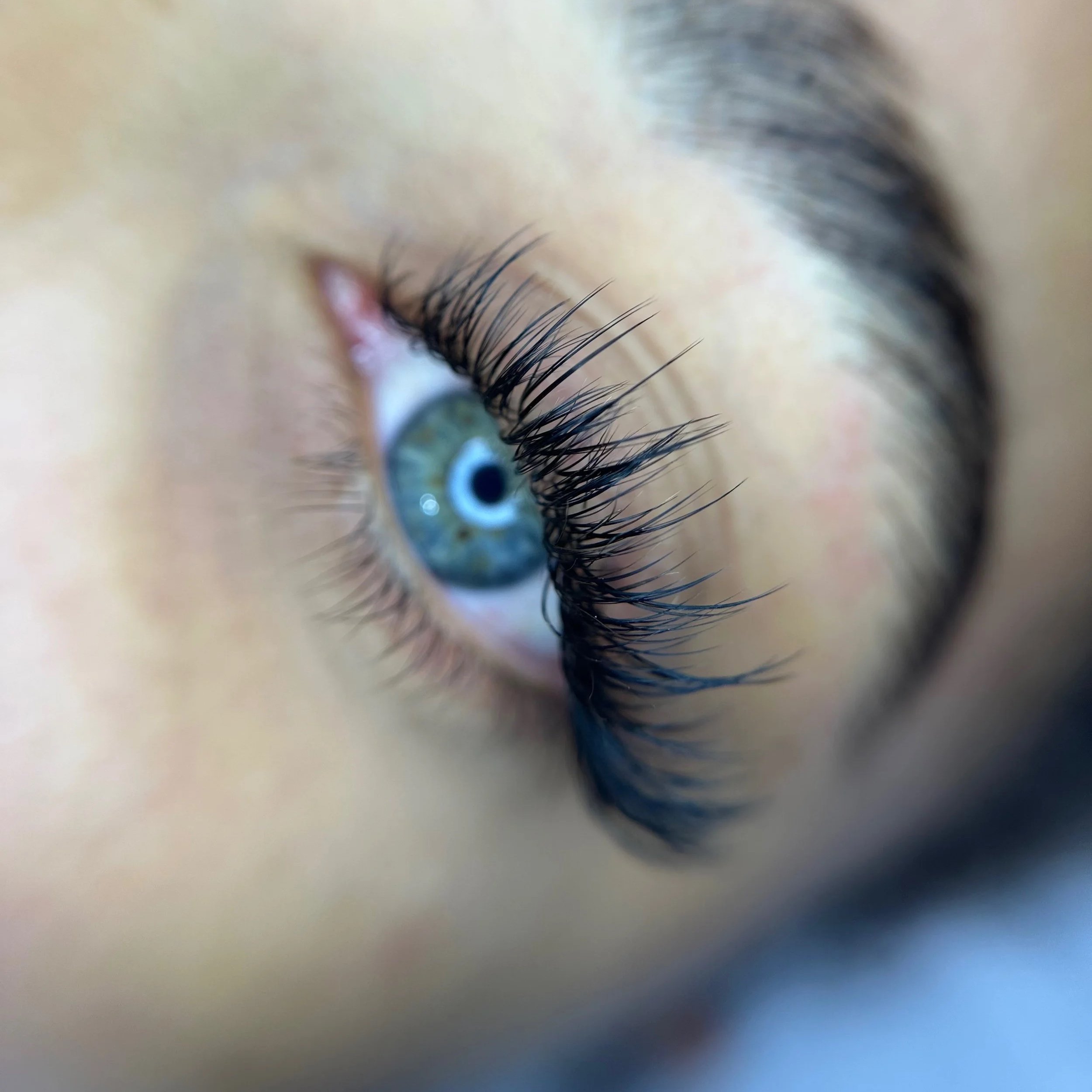Close-up of a person's eye with blue iris, long eyelashes, and light surrounding skin.