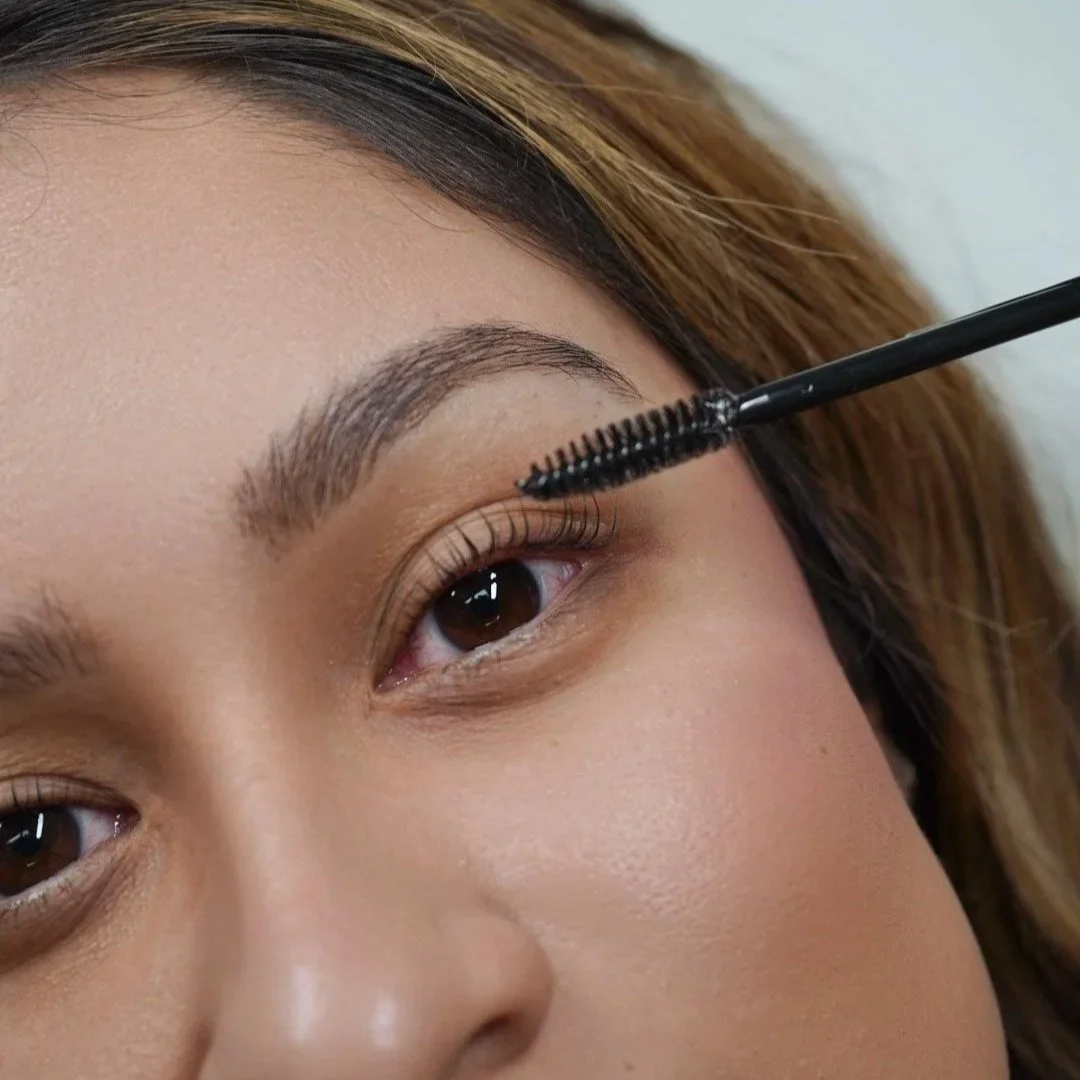 Close-up of a woman applying mascara to her upper eyelashes with a mascara wand.