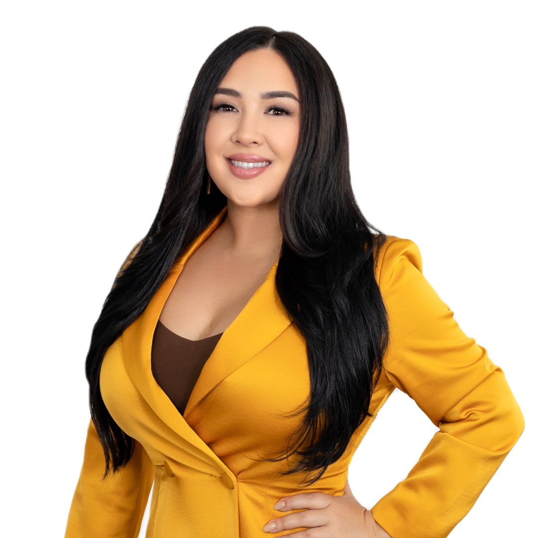 A woman with long black hair in a yellow blazer and brown top, smiling confidently with one hand on her waist.