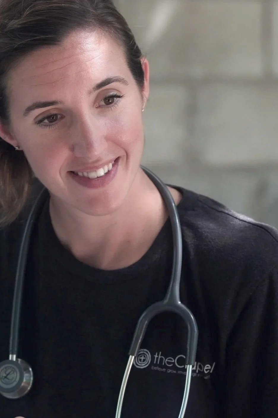 A smiling woman wearing a black shirt with a stethoscope around her neck.