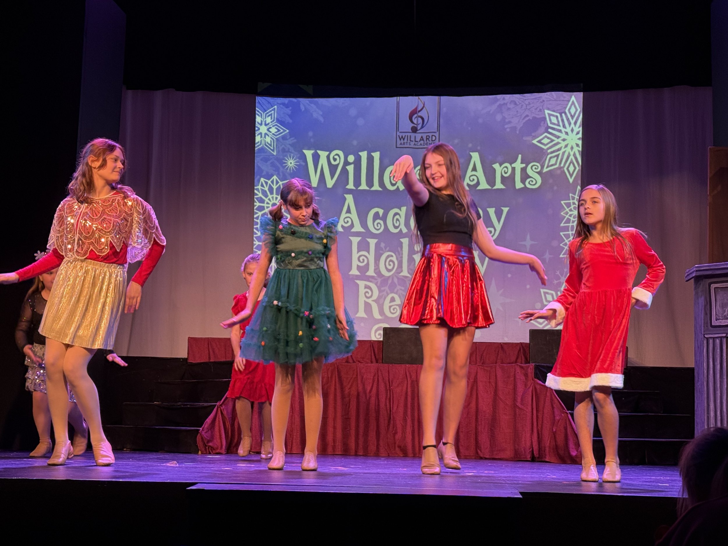 Children performing on stage dressed in festive holiday costumes during a holiday show at Willard Arts Academy.