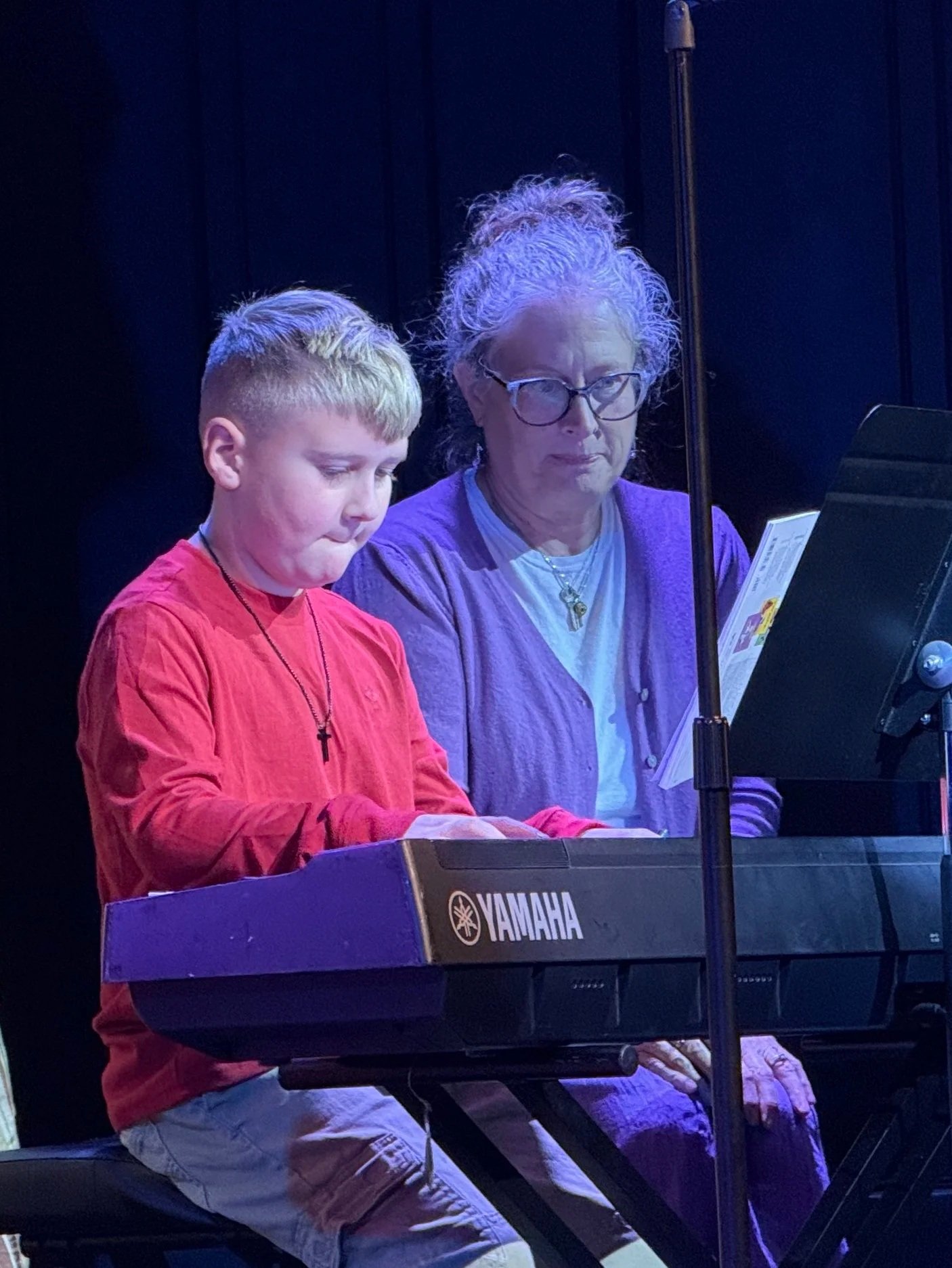 A young boy and an elderly woman playing a Yamaha keyboard together on stage.