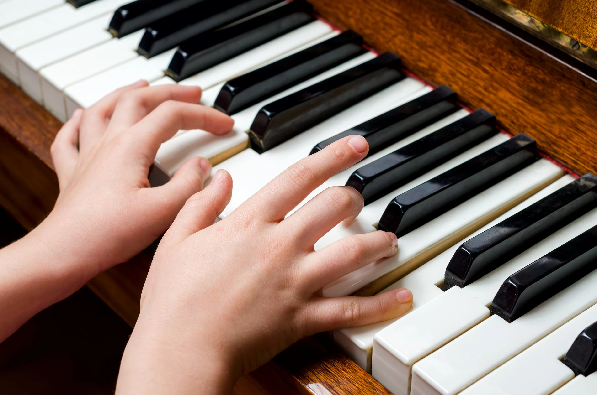 Child's hands playing piano on keyboard with black and white keys.