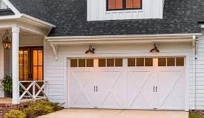 White garage door with black handles, part of a house with black roof shingles and white siding, and a window with a grid pattern.