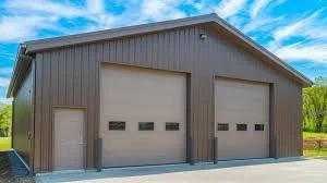 Gray metal storage building with three garage doors and a side door, set on a concrete pad with green trees and a blue sky in the background.