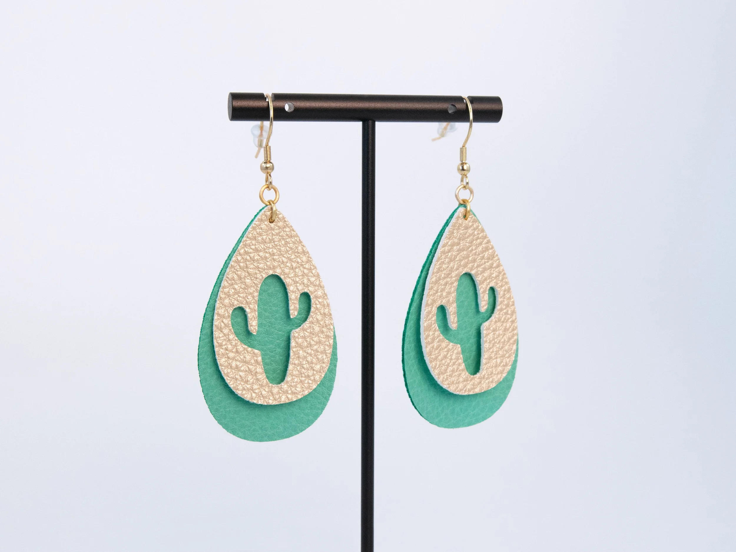 Cactus teardrop earrings on a T-bar display stand. The earrings have layered green and gold faux leather with gold-finished hooks