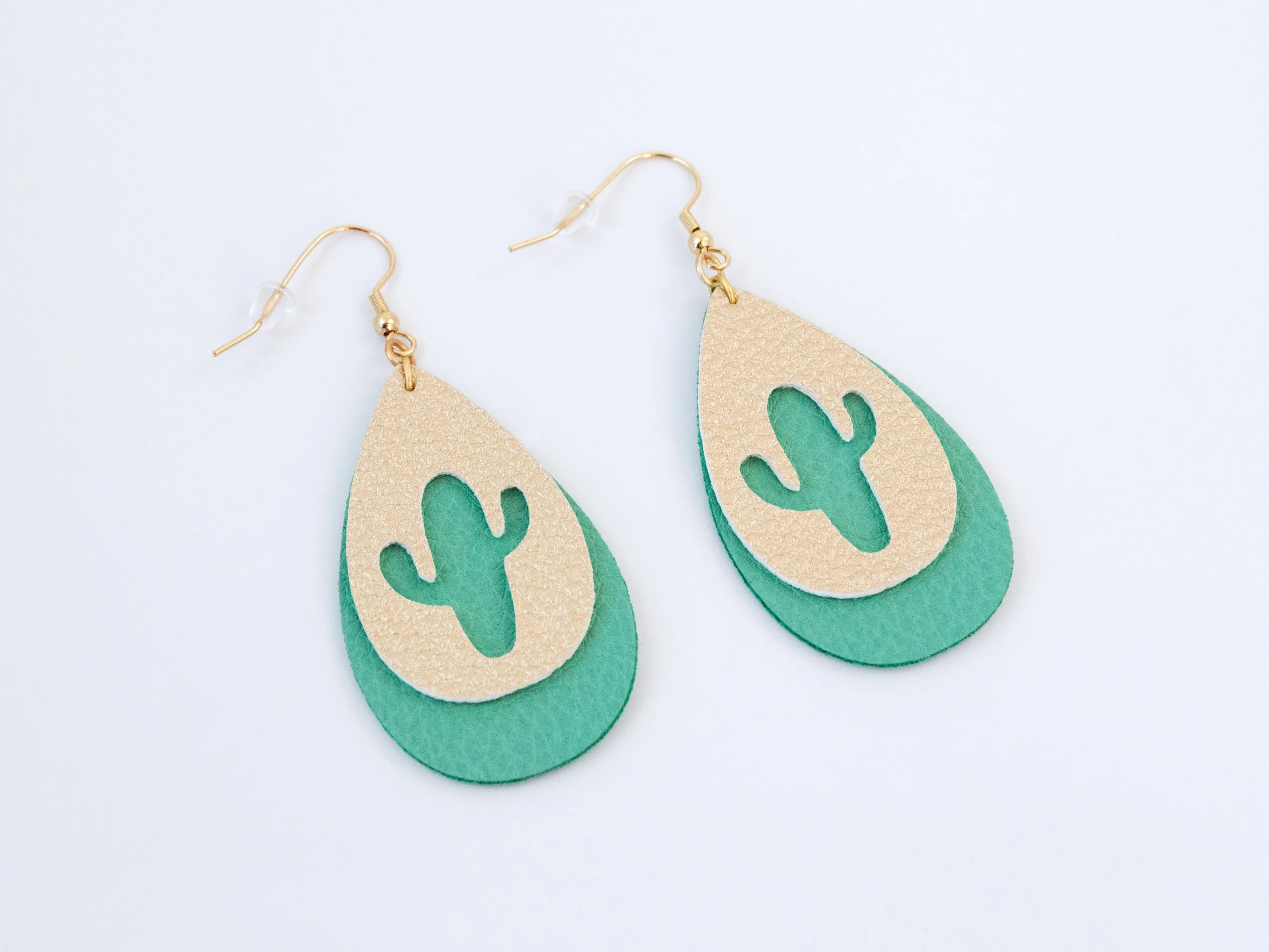 Angled view of cactus teardrop earrings. They have layered green and gold faux leather with gold-finished hooks