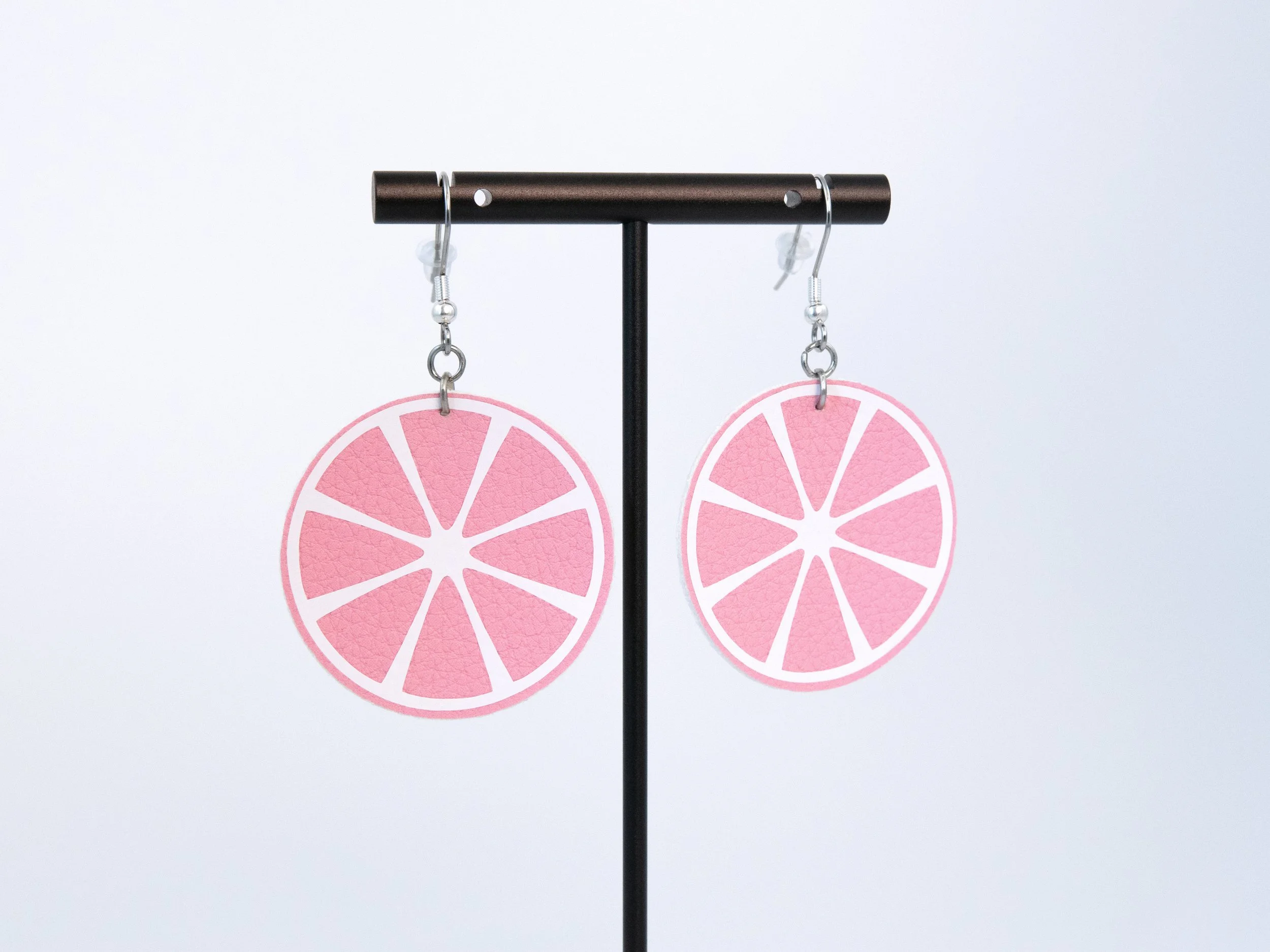 Round citrus slice earrings on a T-bar display stand. The earrings have pink faux leather, white vinyl details, and silver-finished hooks