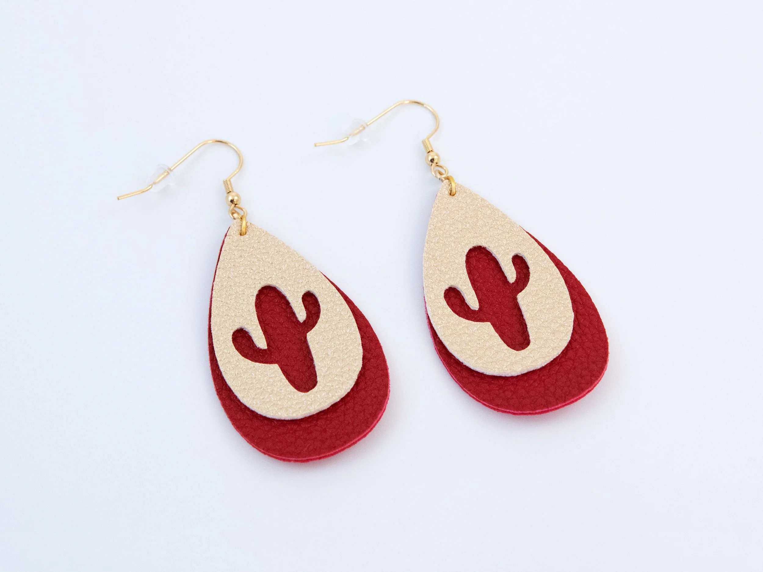 Angled view of cactus teardrop earrings. They have layered red and gold faux leather with gold-finished hooks
