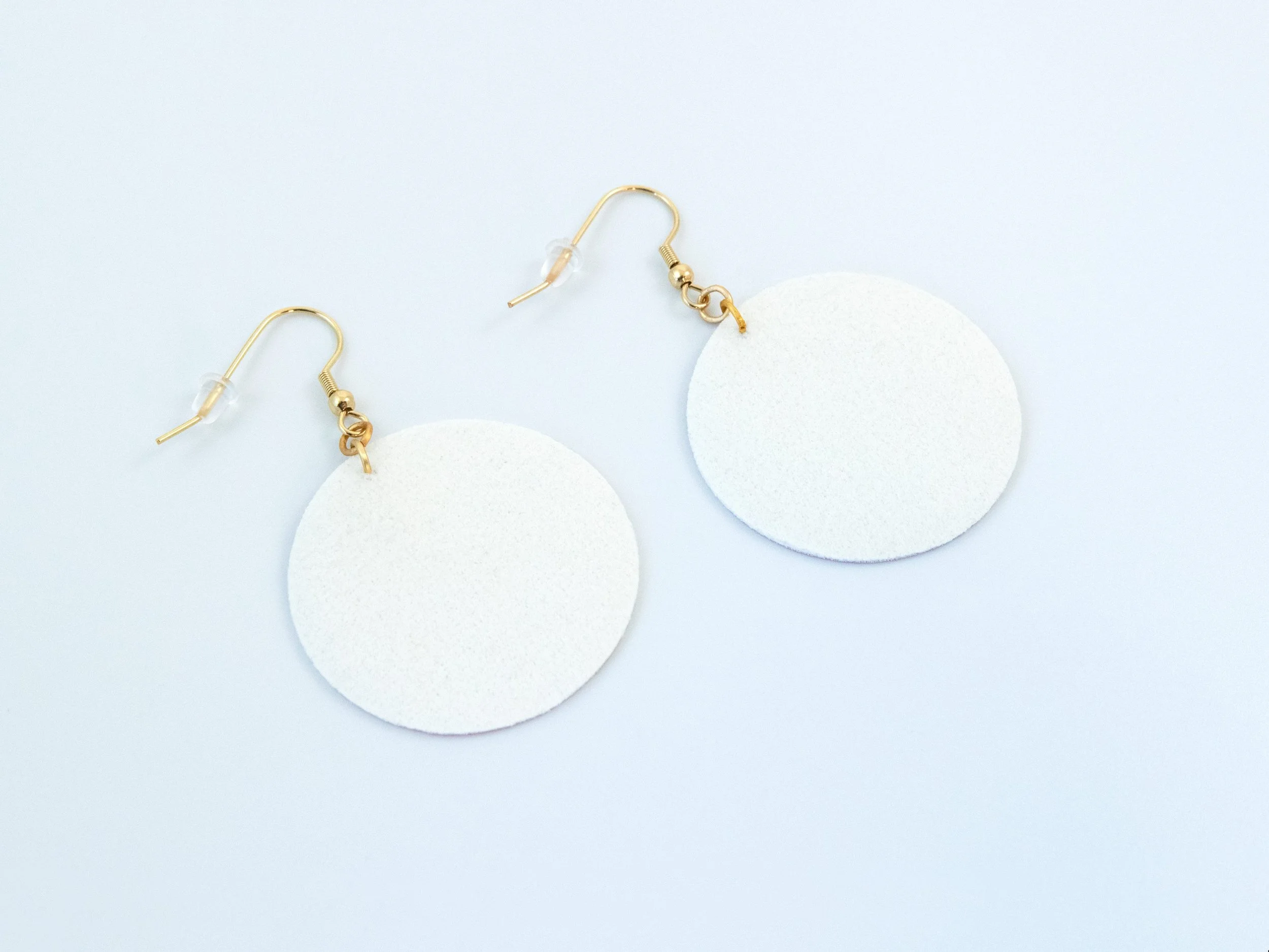 Round pink citrus earrings that have been flipped over. The faux leather fabric is white on the back. The hooks have a gold finish