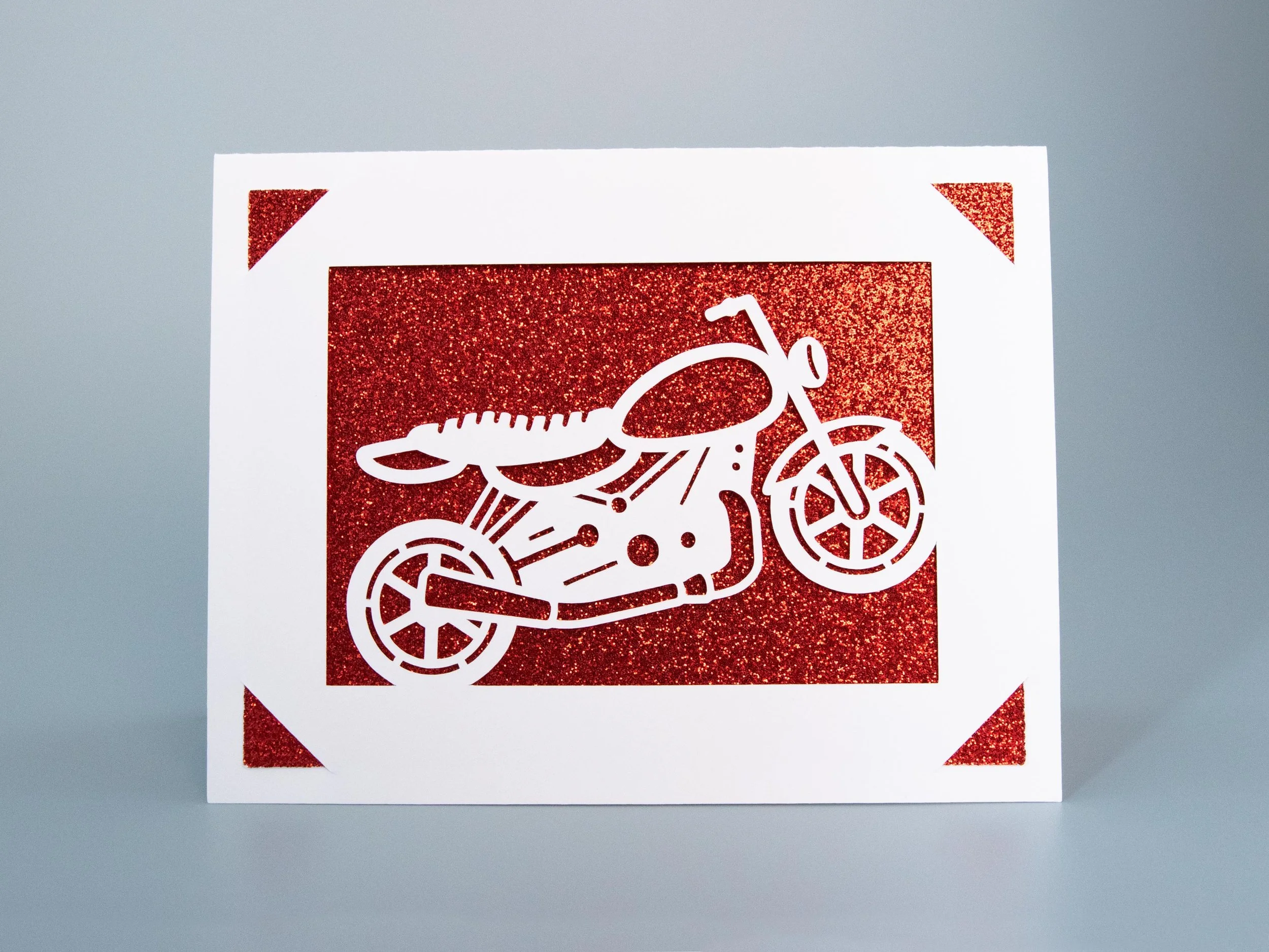 Front view of a greeting card with a motorcycle cutout and red glitter background