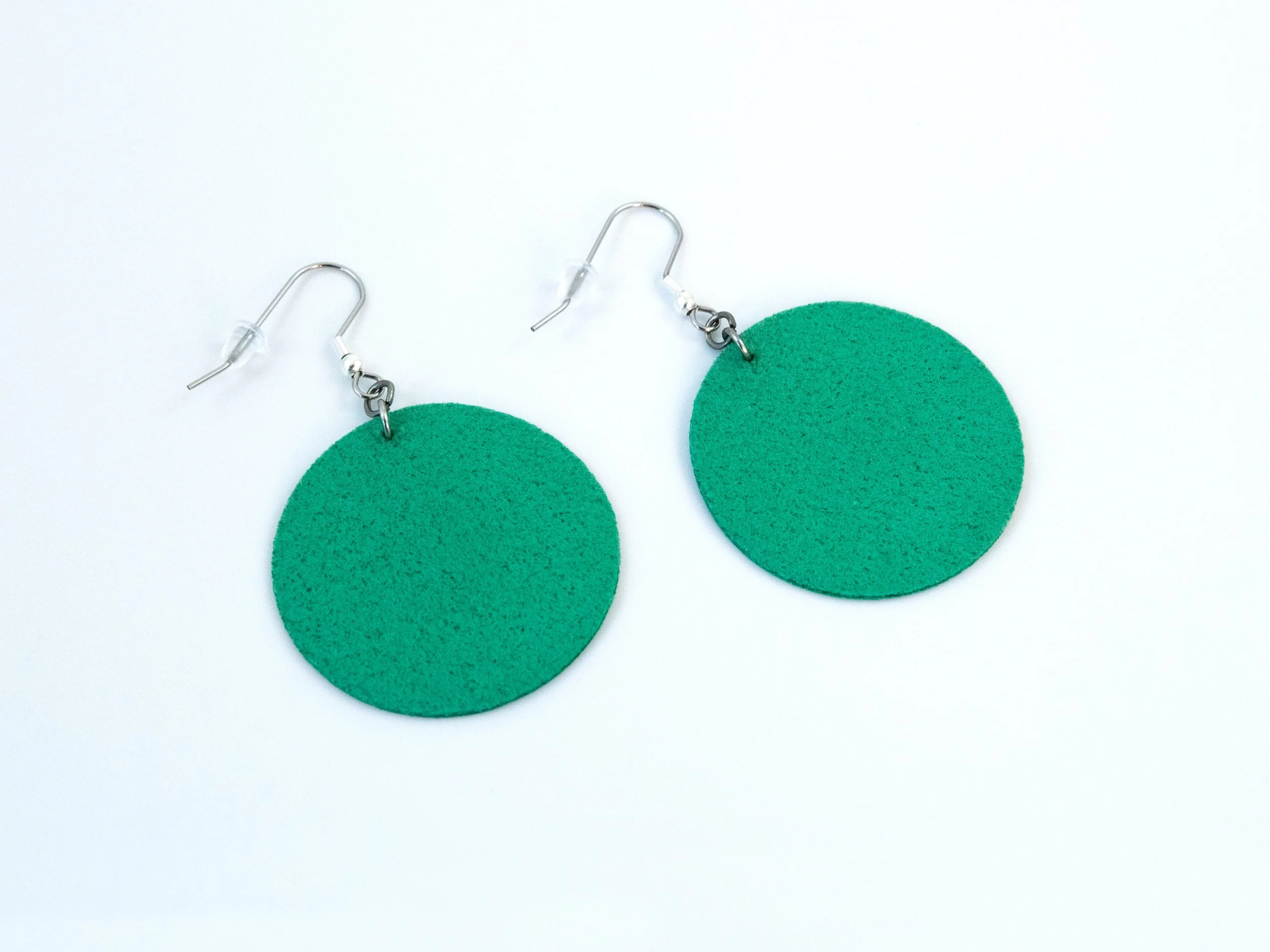 Round green citrus earrings that have been flipped over. The faux leather fabric is also green on the back. The hooks have a silver finish