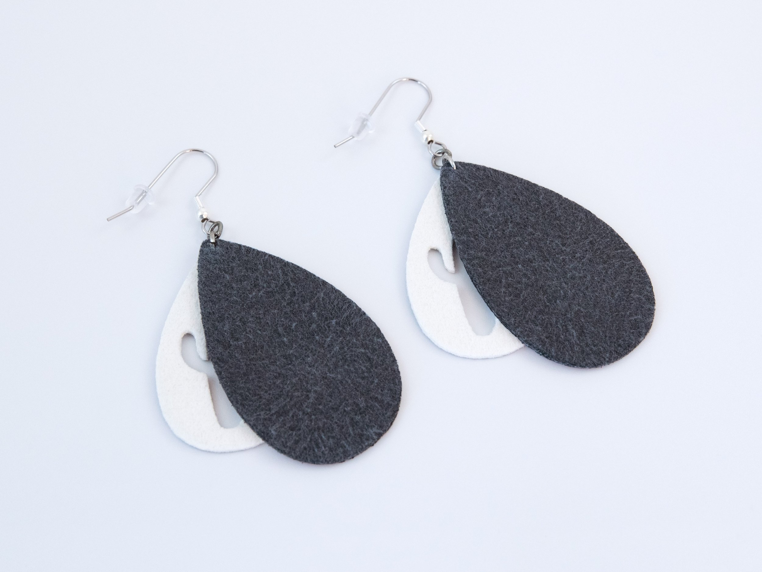 Dark brown and silver cactus teardrop earrings that have been flipped over. Silver faux leather has white fabric on the back, while dark brown faux leather has black fabric on the back