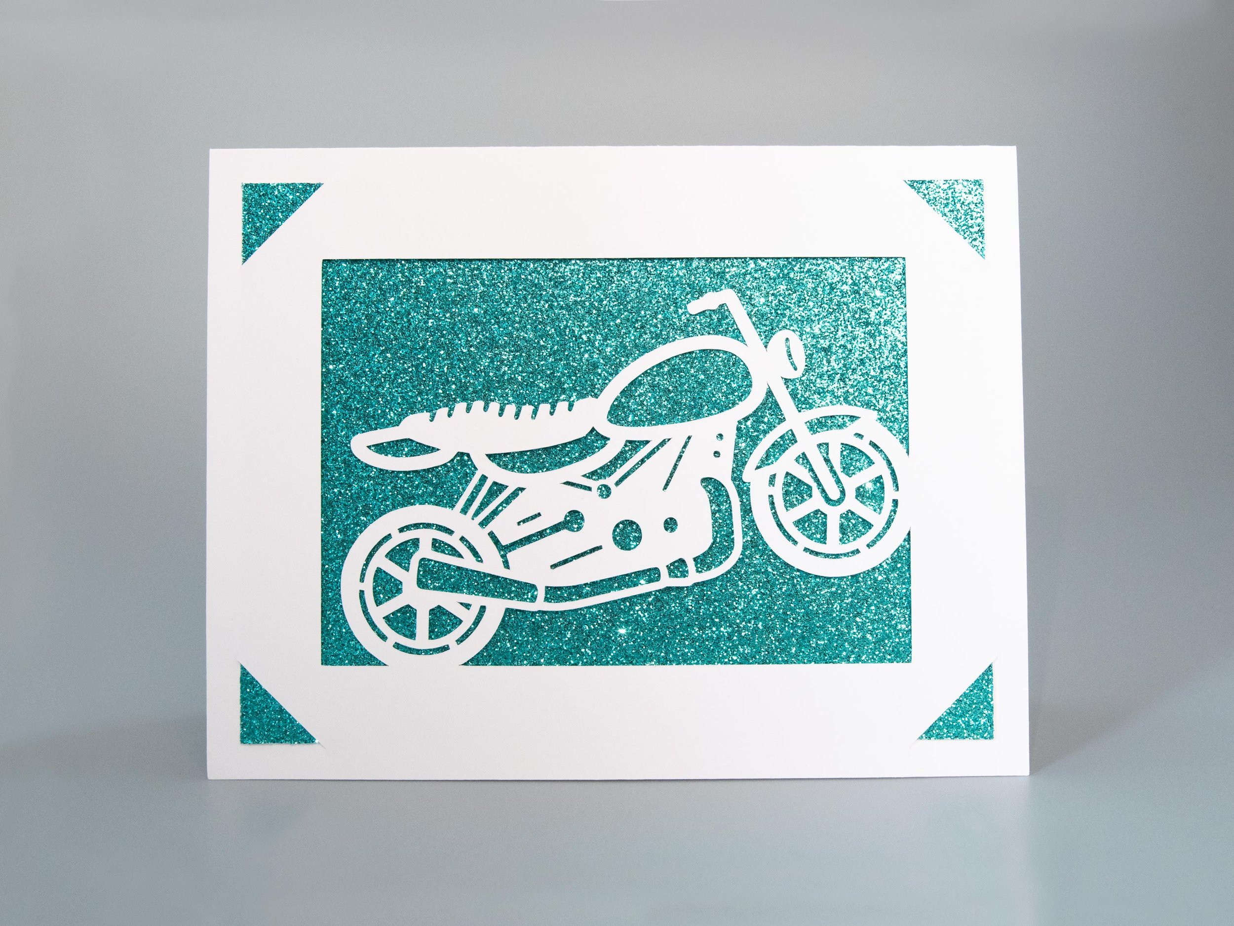 Front view of a greeting card with a motorcycle cutout and turquoise glitter background