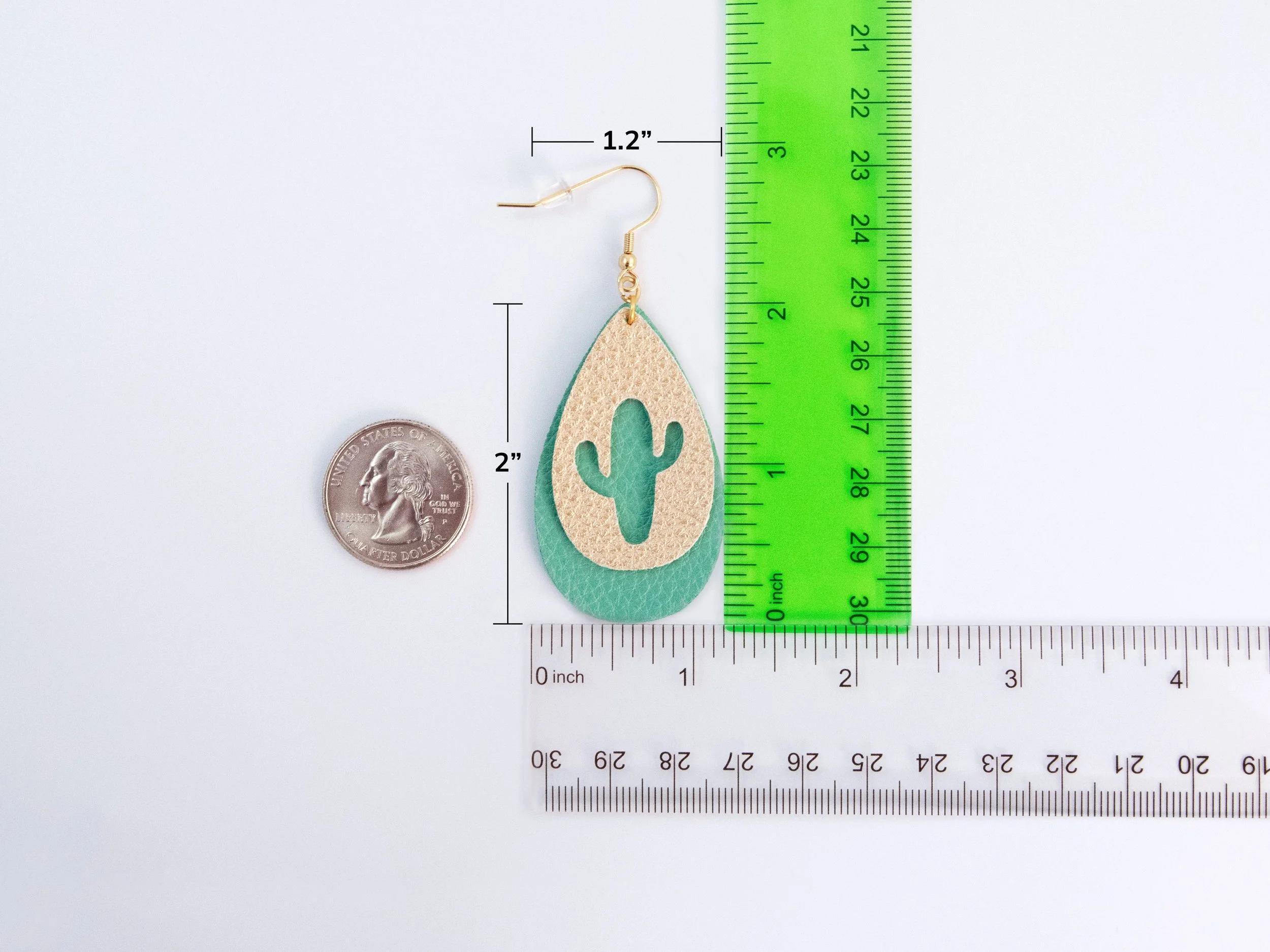A cactus teardrop earring next to rulers and a quarter to show scale. The teardrop is 1.2” wide and 2” tall, which does not include the hook
