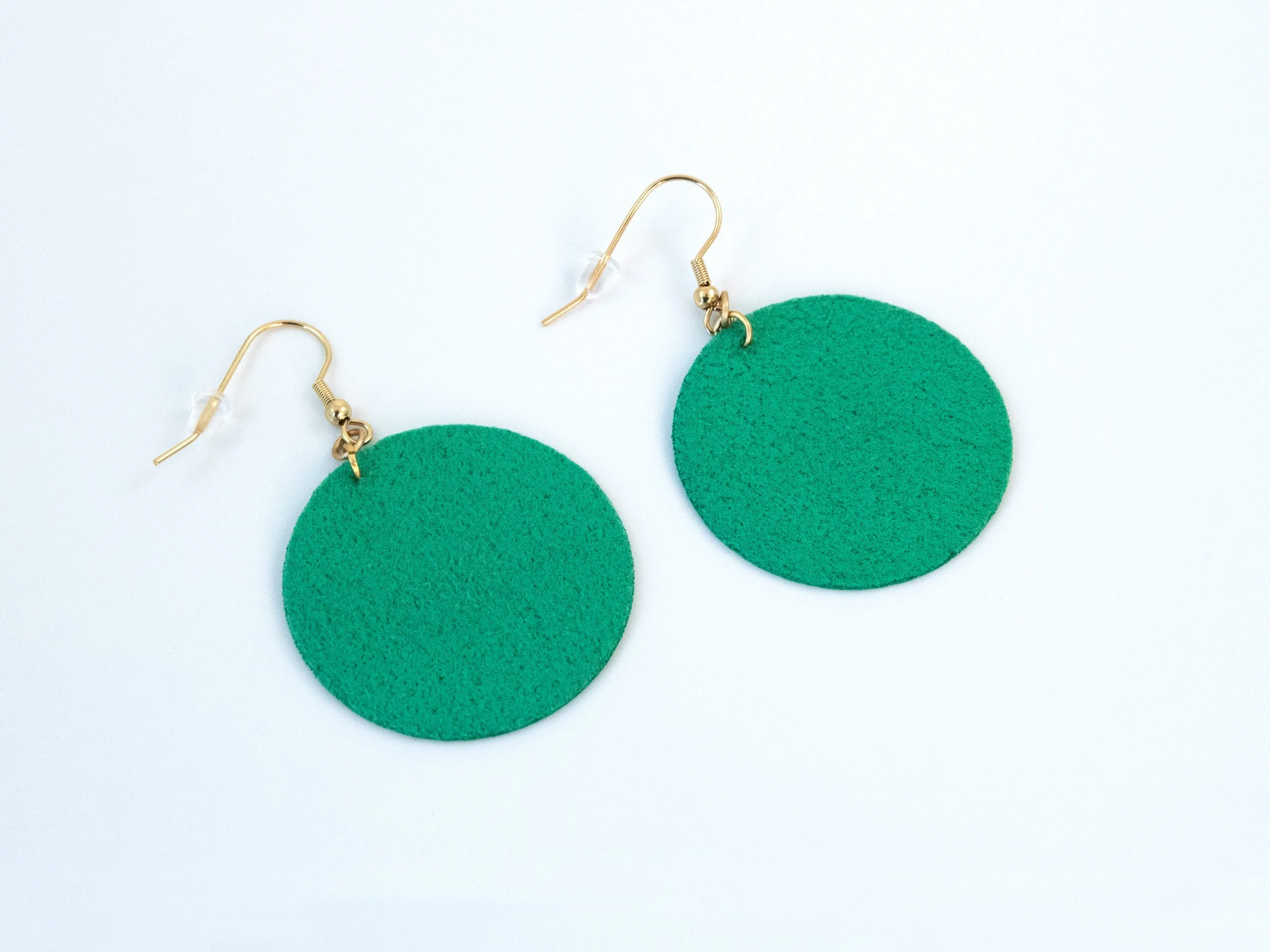 Round green citrus earrings that have been flipped over. The faux leather fabric is also green on the back. The hooks have a gold finish