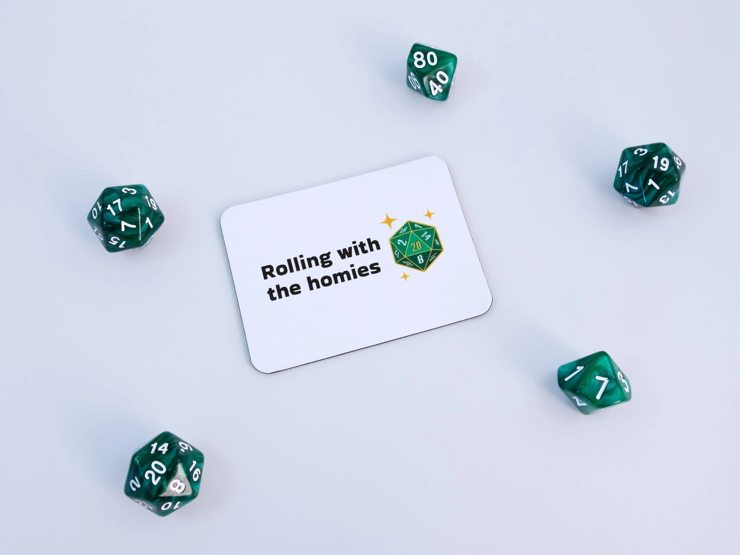 A magnet of a green d20 die with text that says “Rolling with the homies”. The magnet is surrounded by green dice