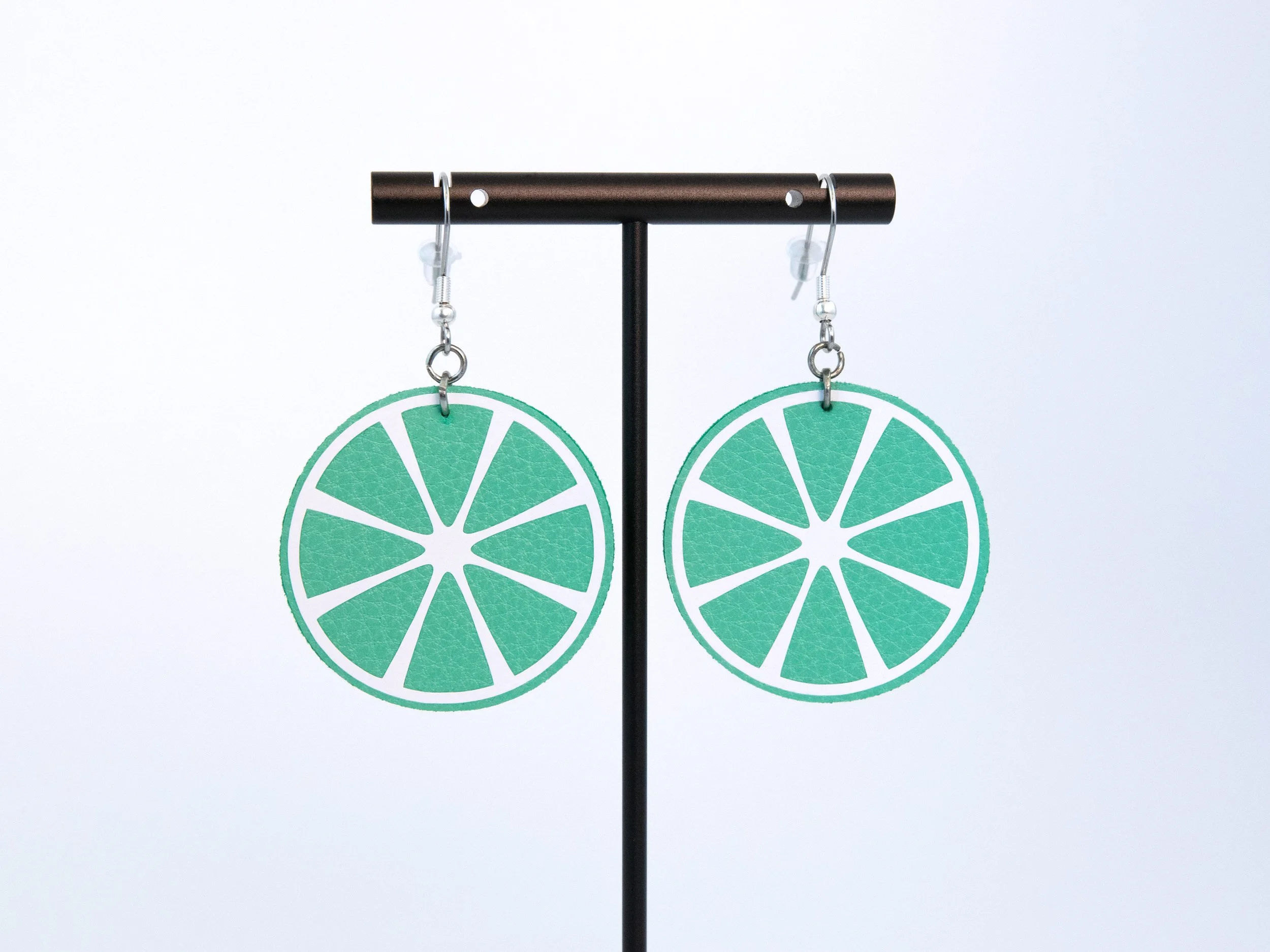 Round citrus slice earrings on a T-bar display stand. The earrings have green faux leather, white vinyl details, and silver-finished hooks