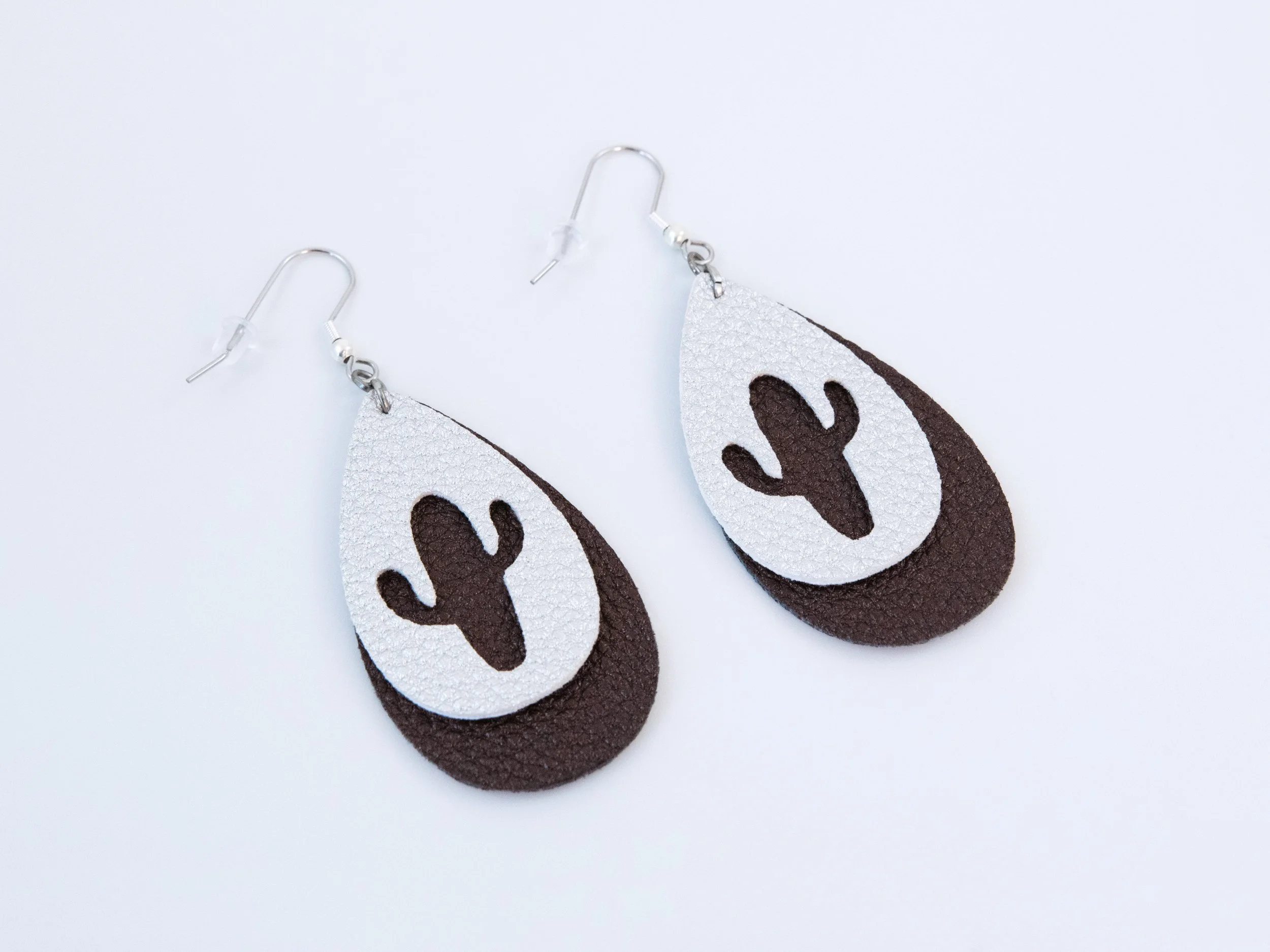 Angled view of cactus teardrop earrings. They have layered dark brown and silver faux leather with silver-finished hooks
