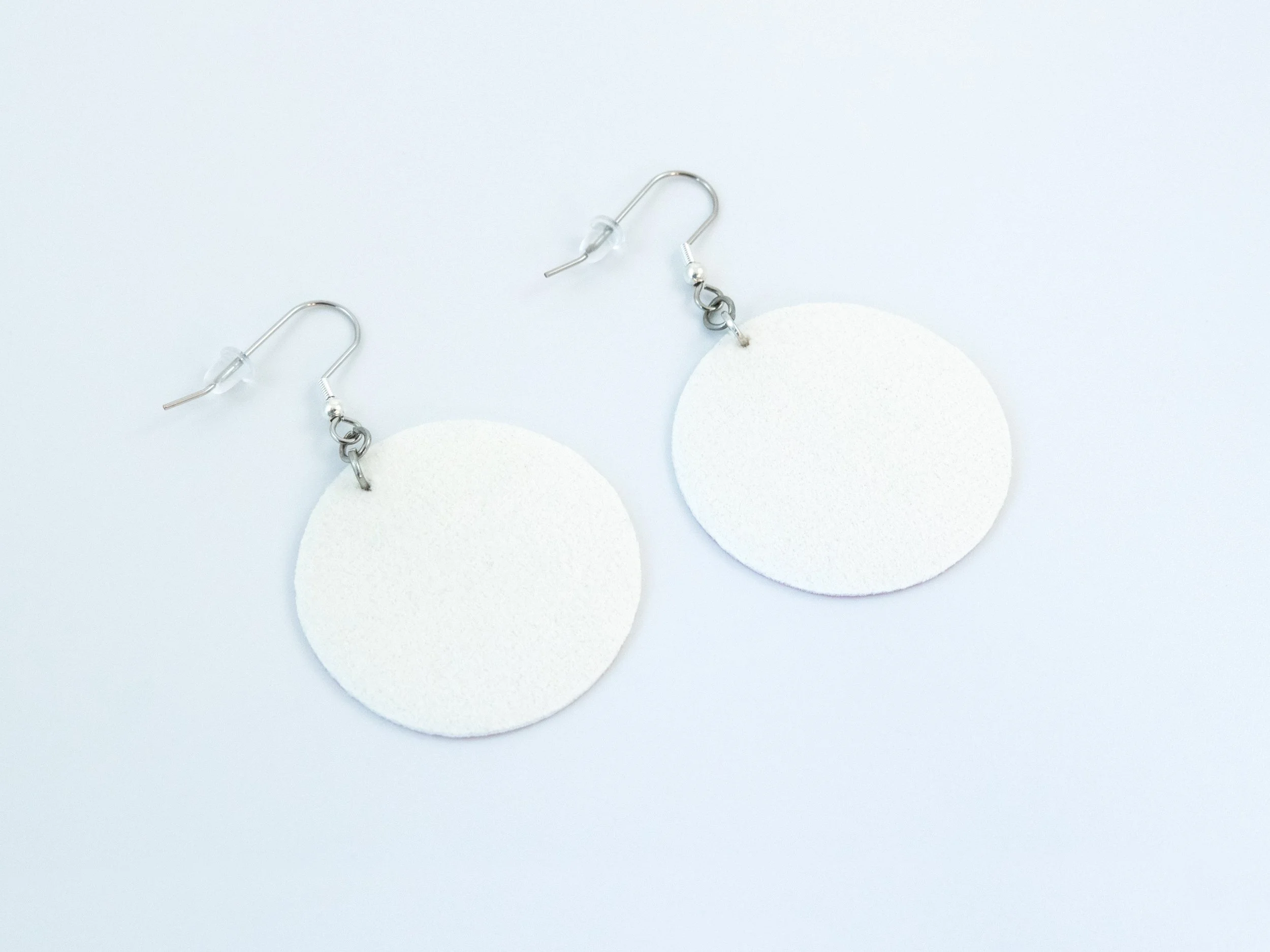 Round pink citrus earrings that have been flipped over. The faux leather fabric is white on the back. The hooks have a silver finish