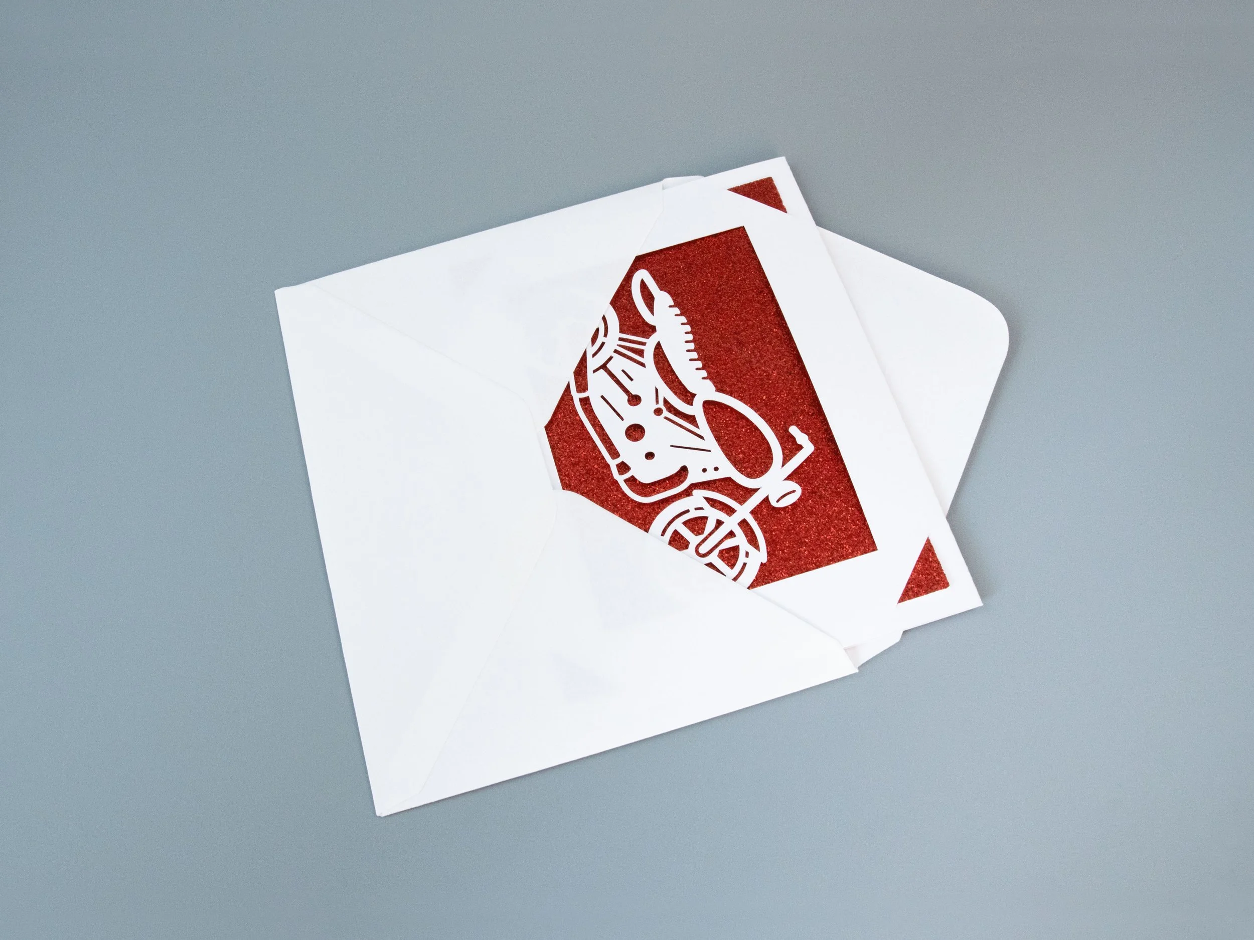 A greeting card partially removed from an envelope. The card has a motorcycle cutout and red glitter background