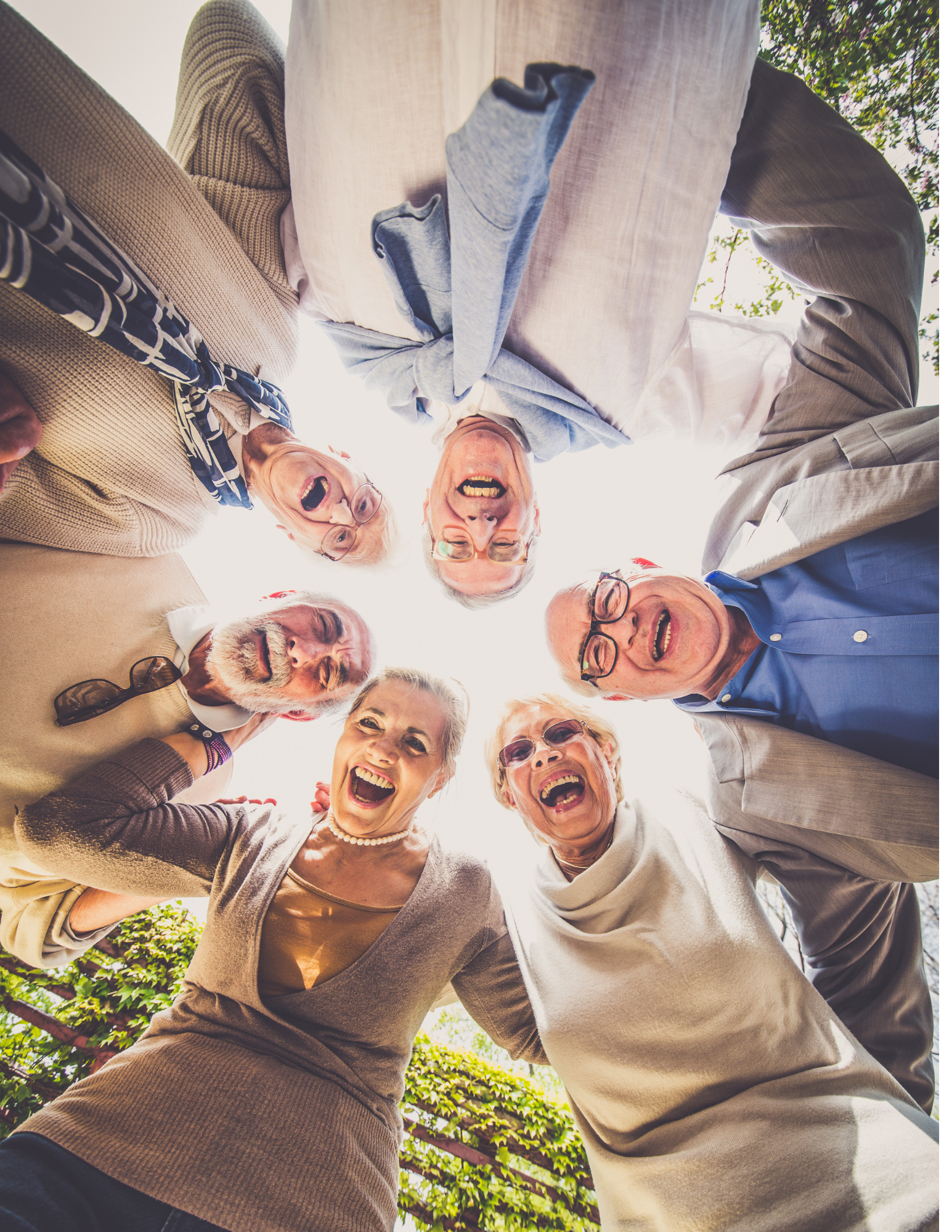 A group of elderly friends standing in a circle outdoors, looking down at the camera with joyful expressions.