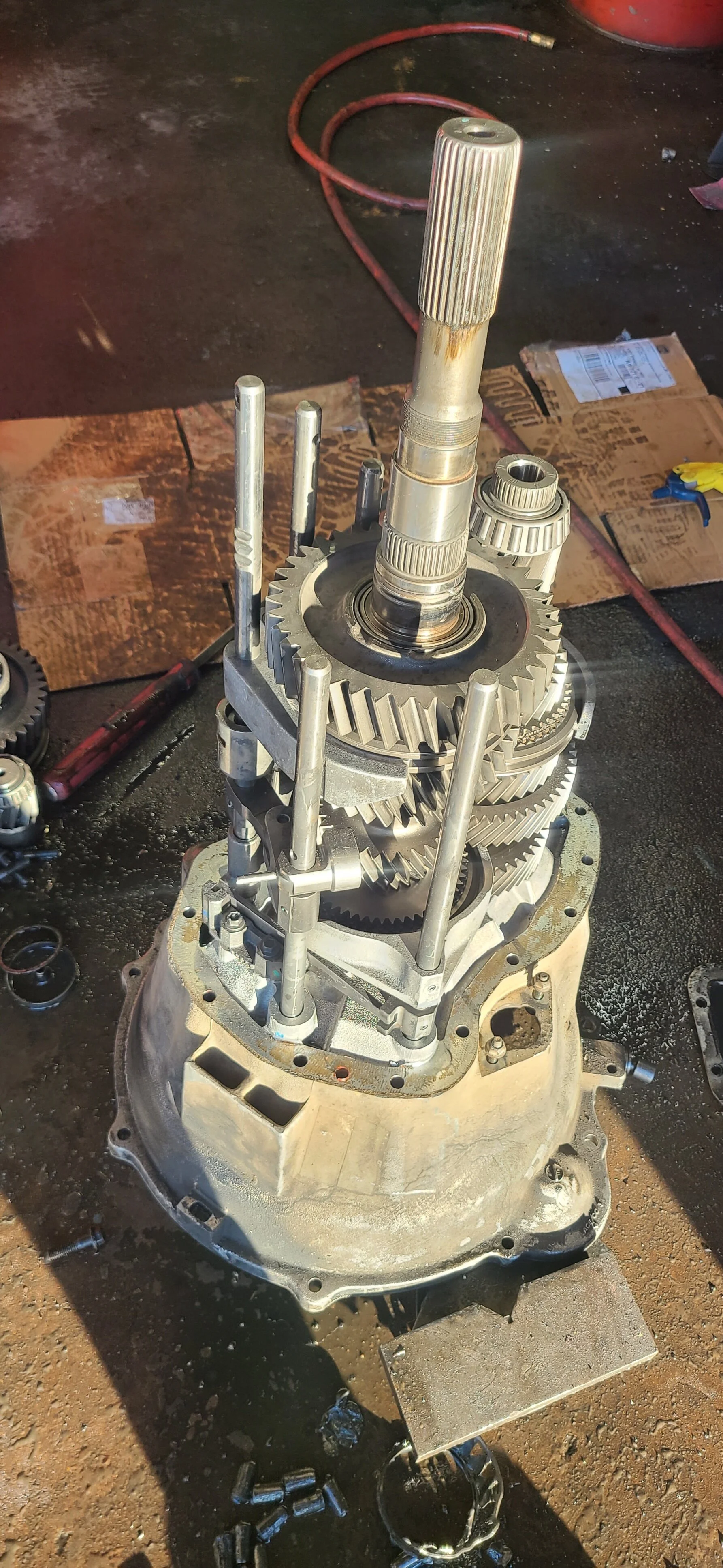 Disassembled gear transmission with metal gears, shafts, and housing on a workshop surface.