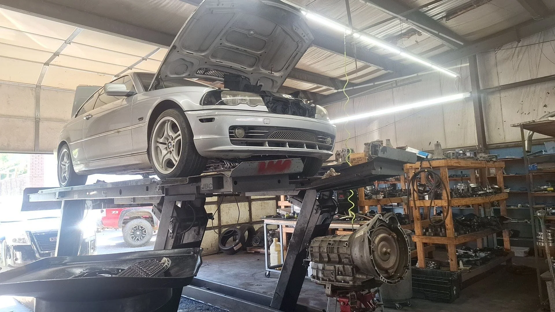 Silver BMW car undergoing repair or maintenance, elevated on a hydraulic lift inside an automotive workshop.