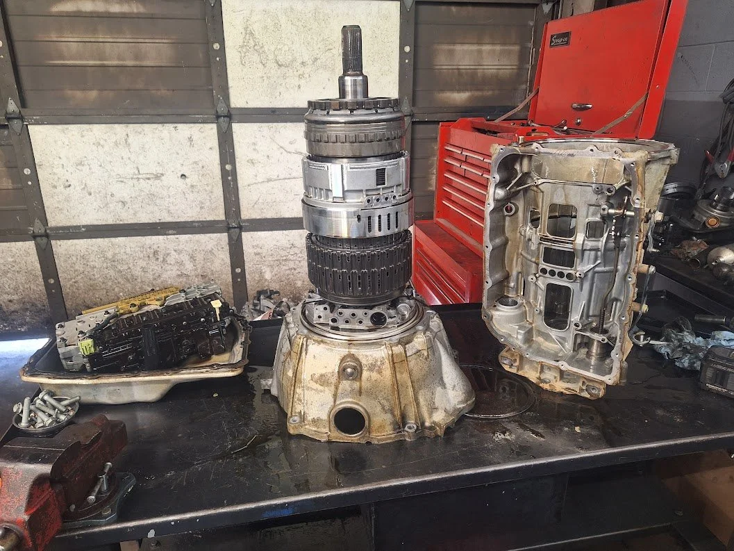 Disassembled complex mechanical gearbox and transmission components on a black workbench in a workshop setting.